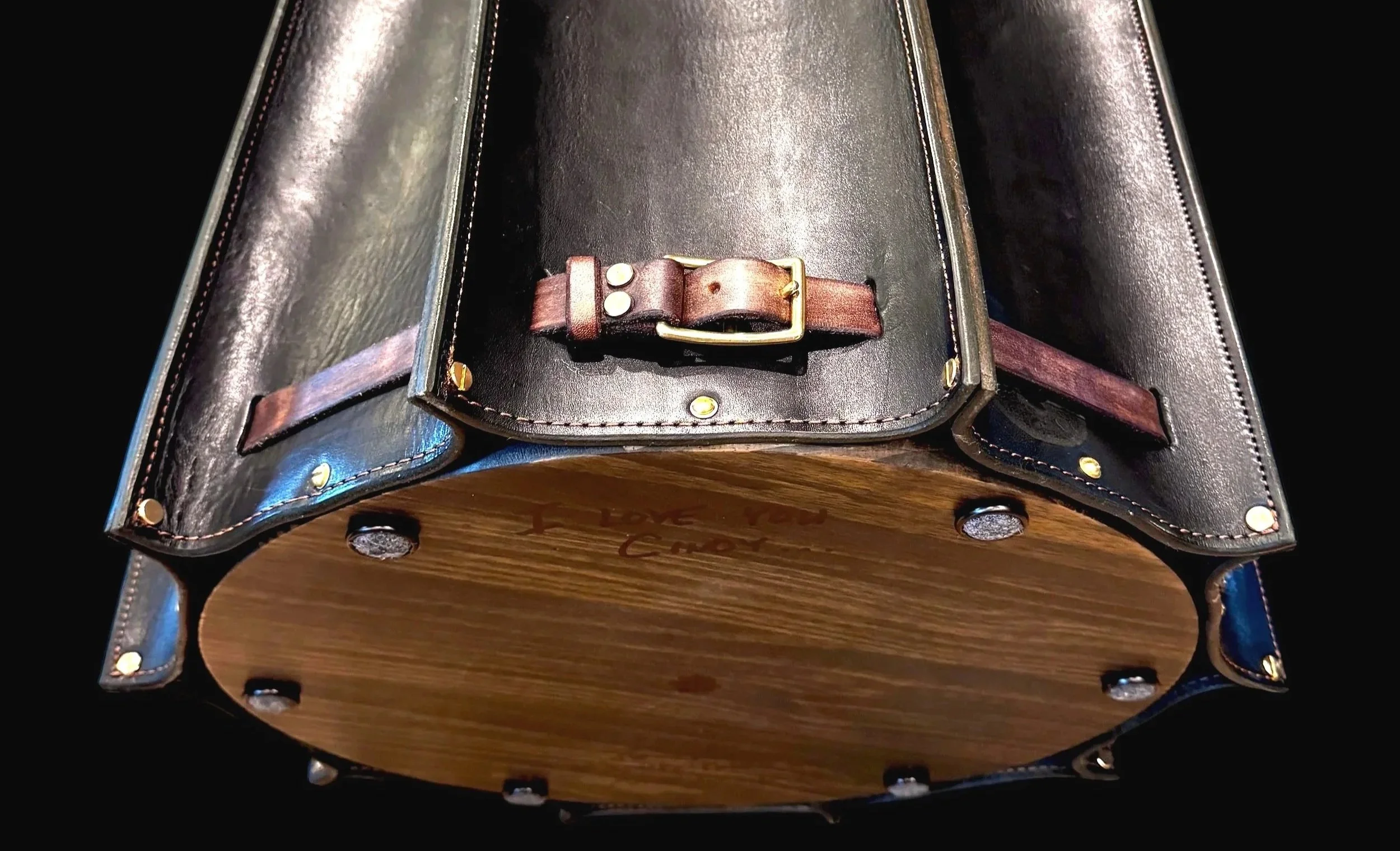 A close-up of a black leather object with metal rivets and a buckle, placed on a wooden base.