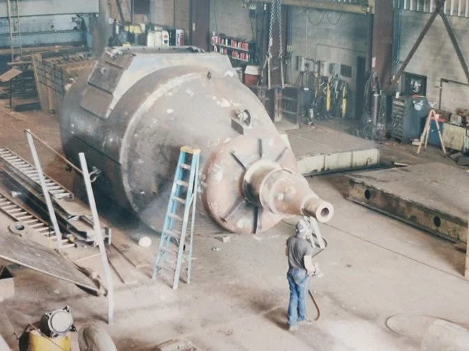A worker inspecting a large, cylindrical industrial tank inside a factory or workshop.