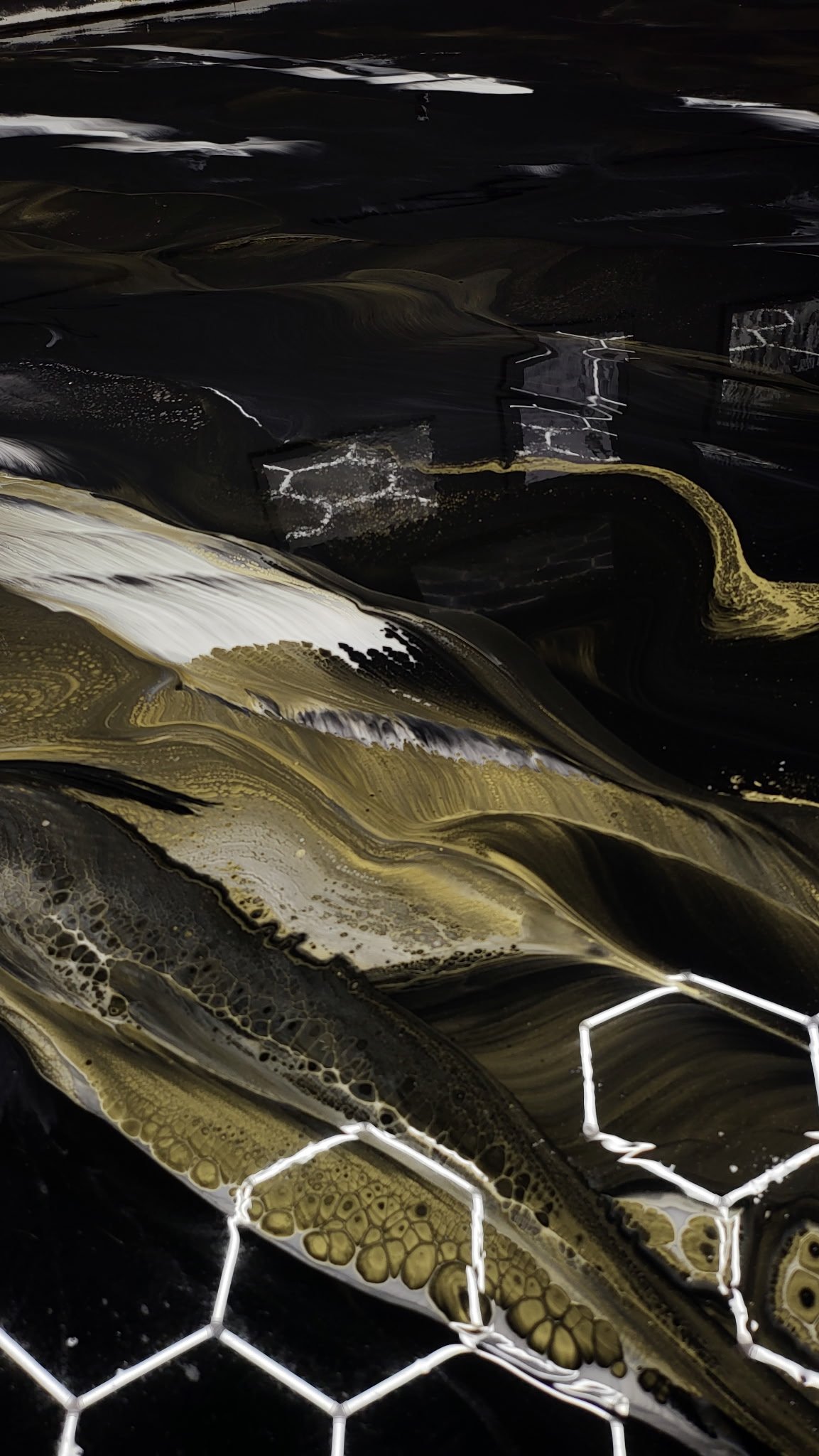 Abstract black, white, and gold swirling fluid art with a white hexagonal wire mesh in the foreground.