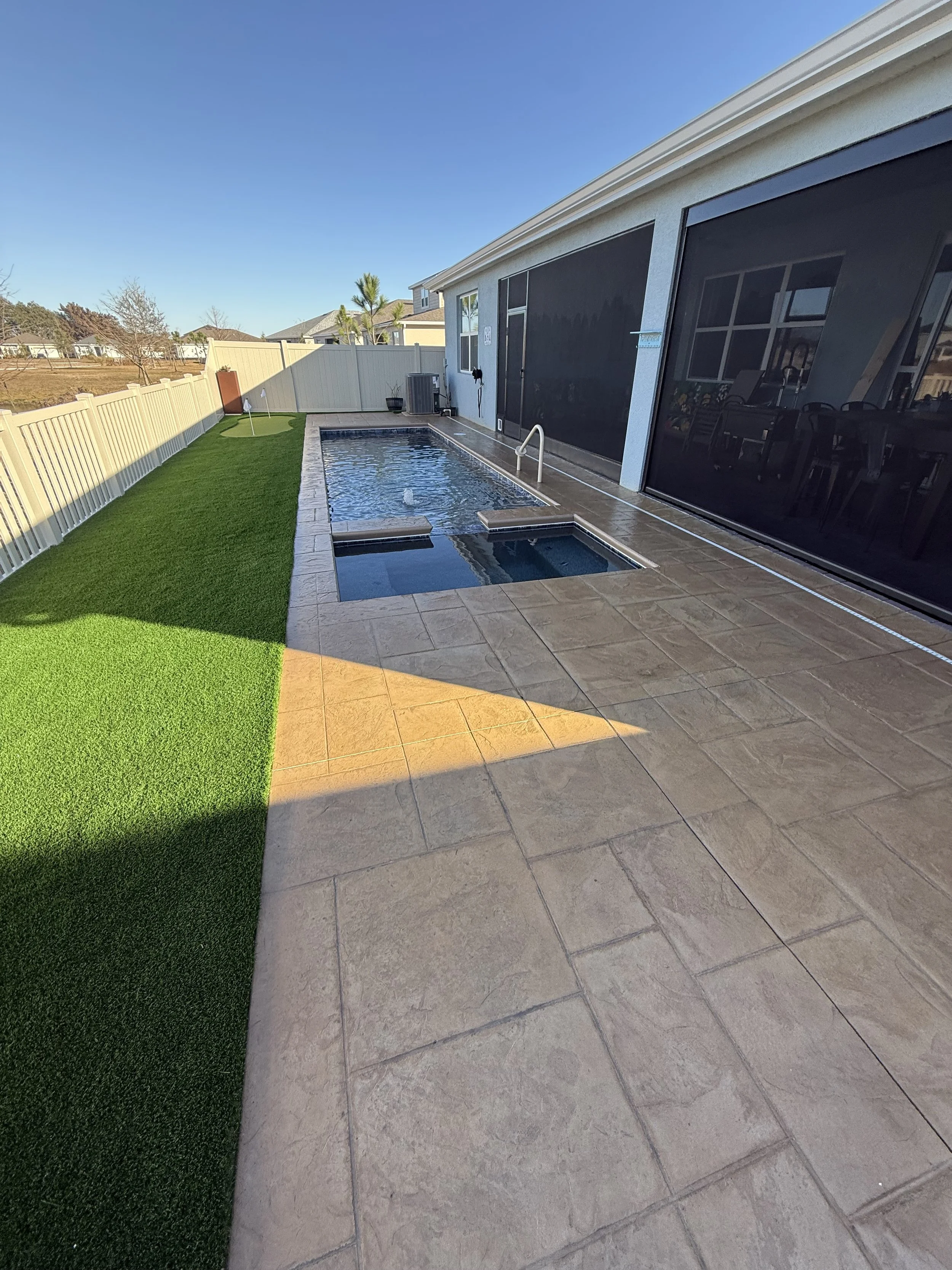 Backyard patio with a small swimming pool, artificial grass, and a white fence.