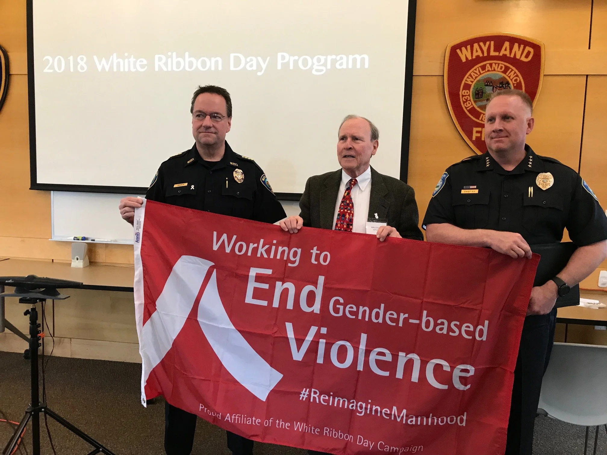 Three men standing at a presentation for the 2018 White Ribbon Day Program.