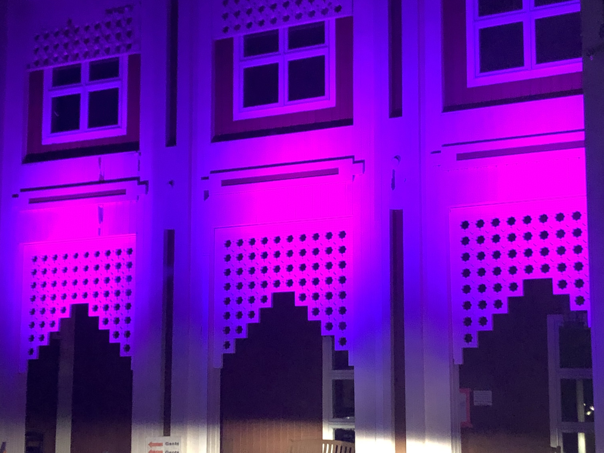 The building's exterior is illuminated with purple and pink lighting, accentuating the geometric window and vent patterns.