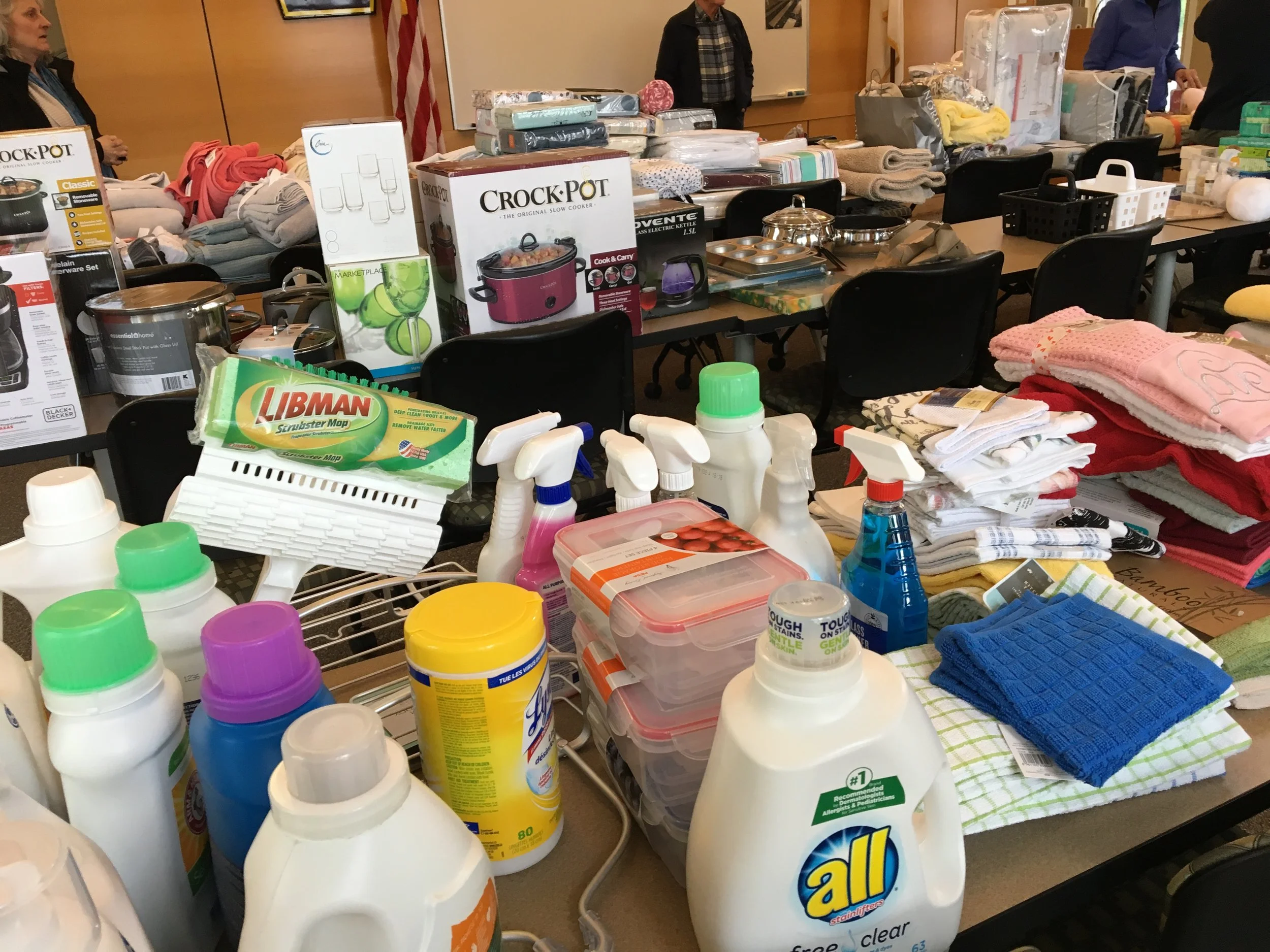 Table filled with cleaning supplies, household items, and folded towels.
