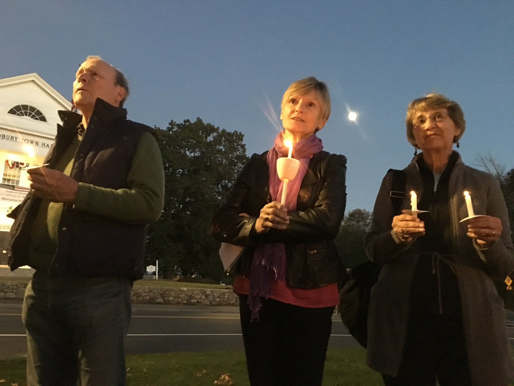 Three women holding candles during an evening outdoor event.