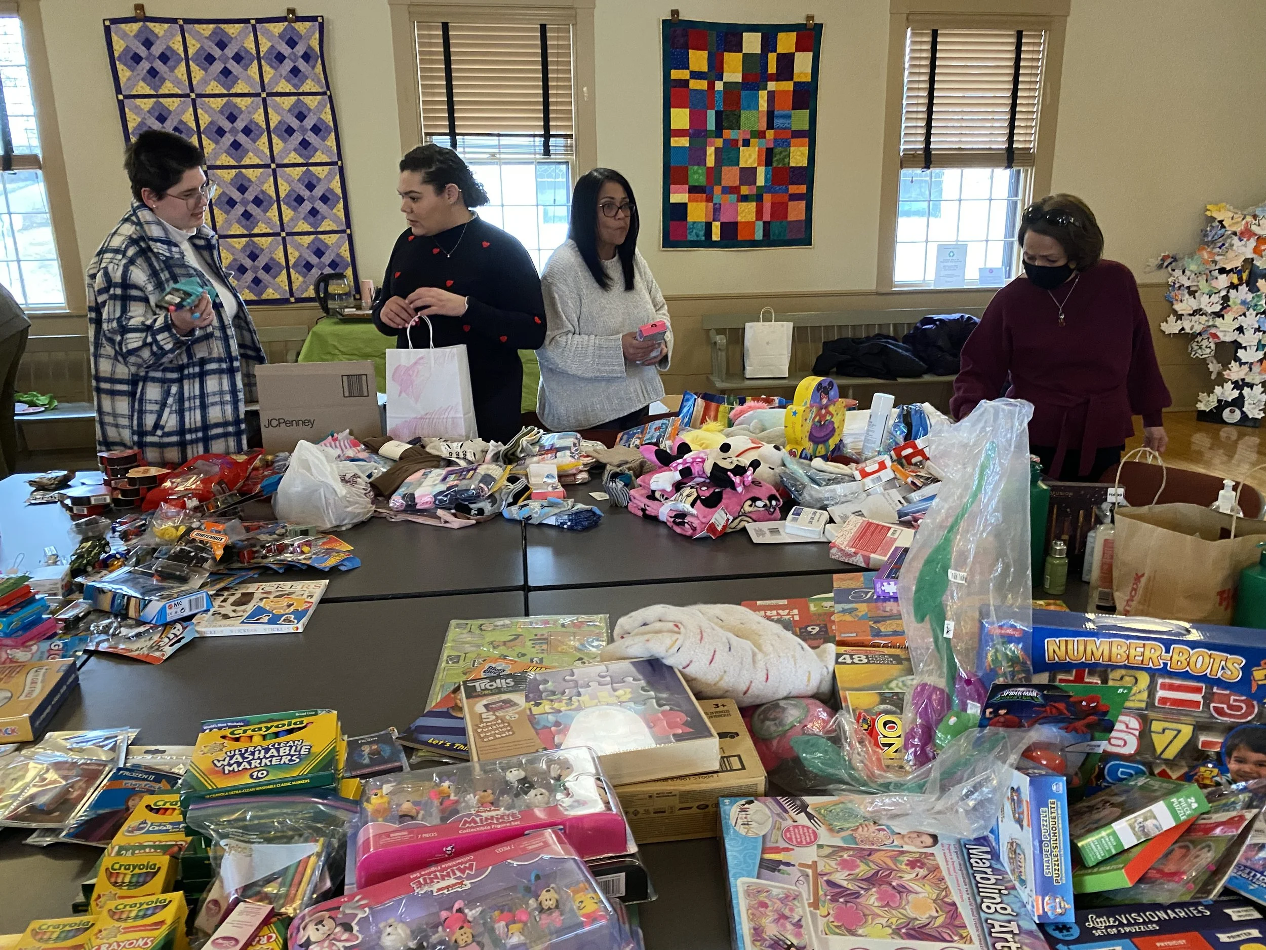 A room with three women filling gift bags, surrounded by various toys, games, and puzzles.