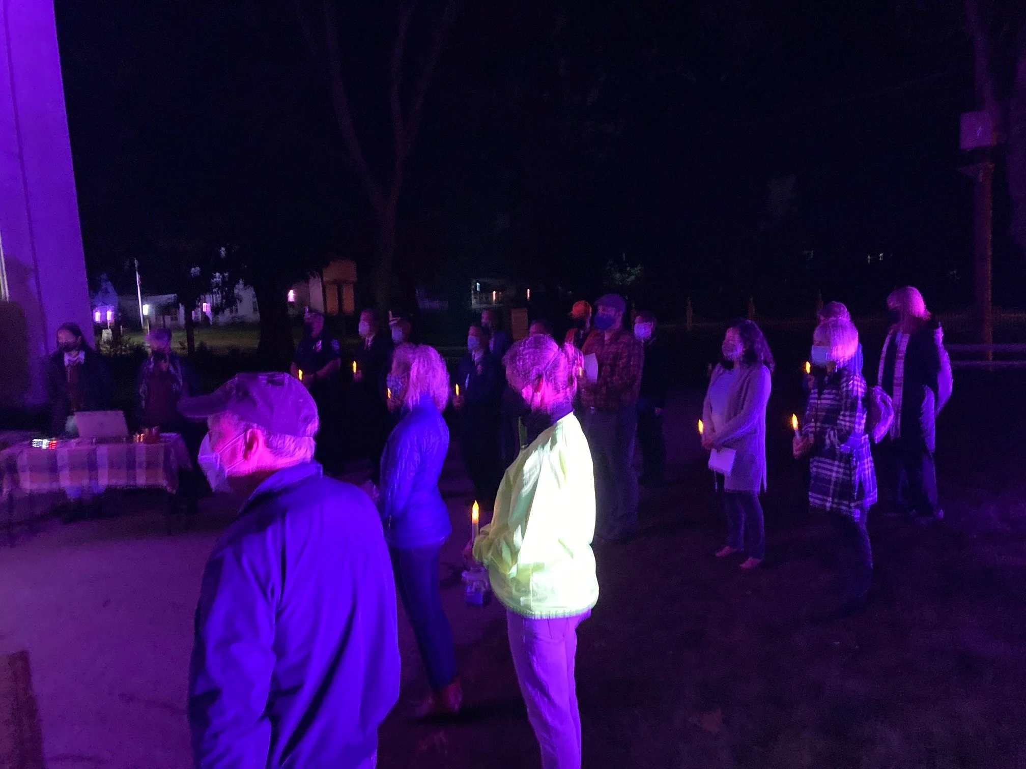 People gathered outside at night, illuminated by purple and blue lights.