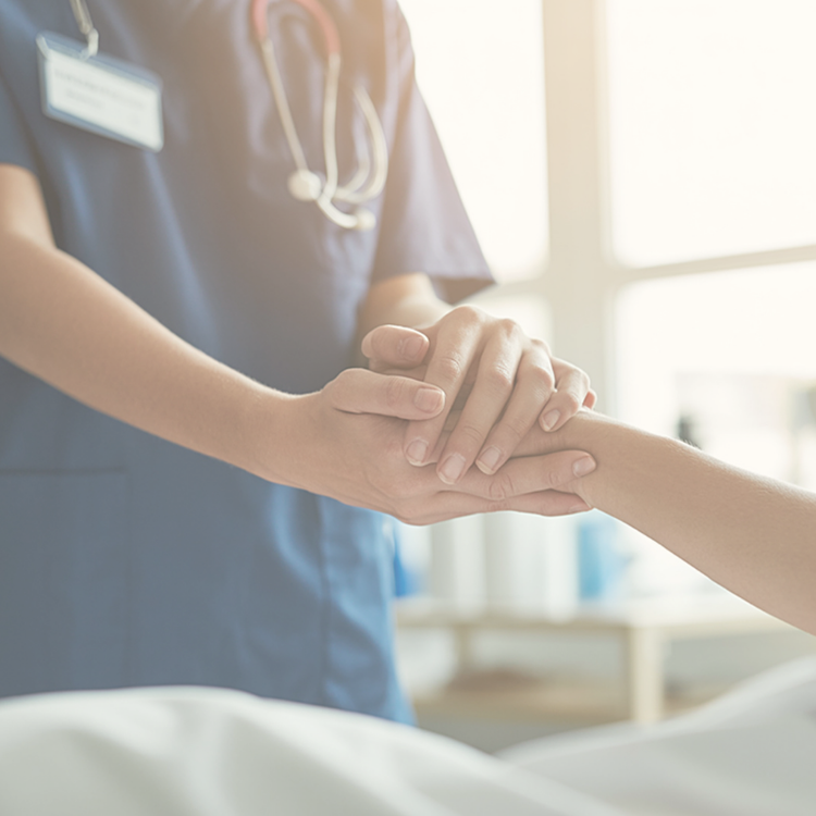 A healthcare professional, wearing scrubs and a stethoscope, holding a patient's hand in a compassionate manner in a medical setting.
