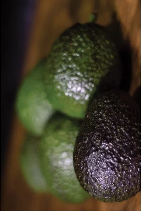 A close-up of three ripe avocados, one green and two dark purple-black, on a wooden surface.