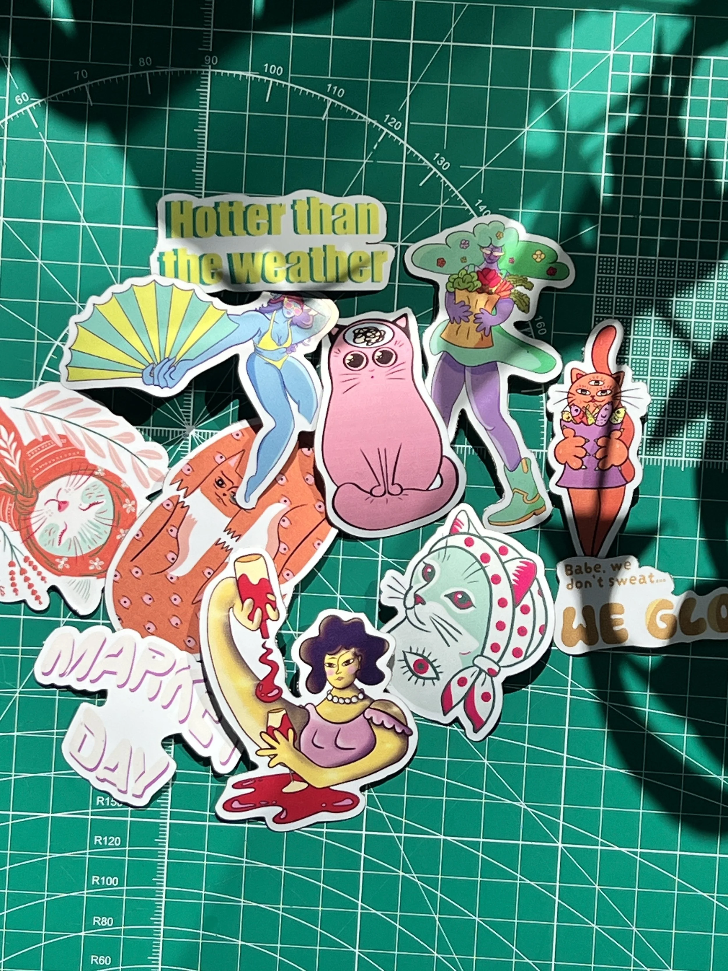 A collection of colorful stickers featuring various characters and phrases, laid out on a green cutting mat with measurement gridlines.