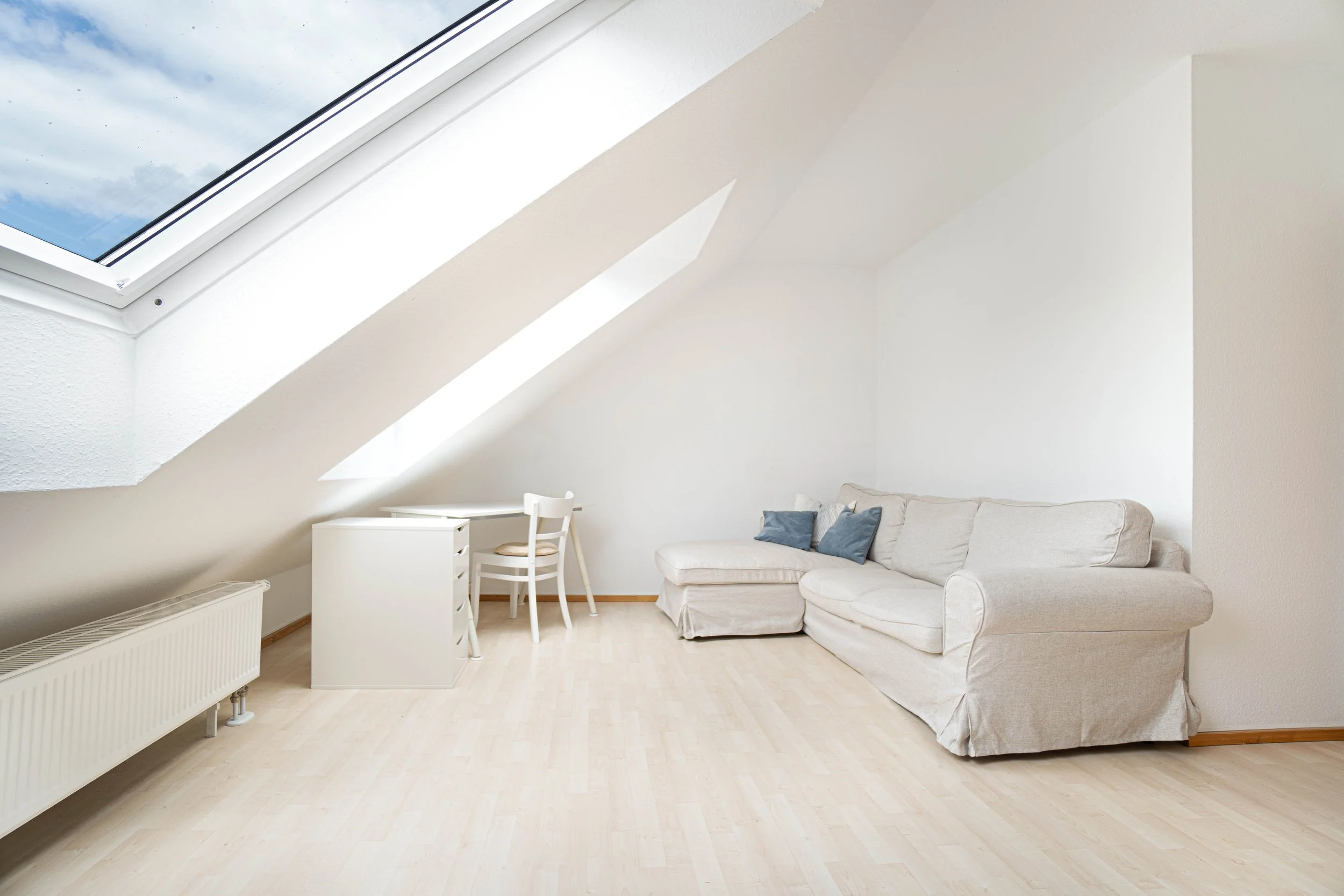 Wohnzimmer mit Weißer Couch, weißen Möbeln, Holzboden, Dachfenster mit Blick auf Wolken