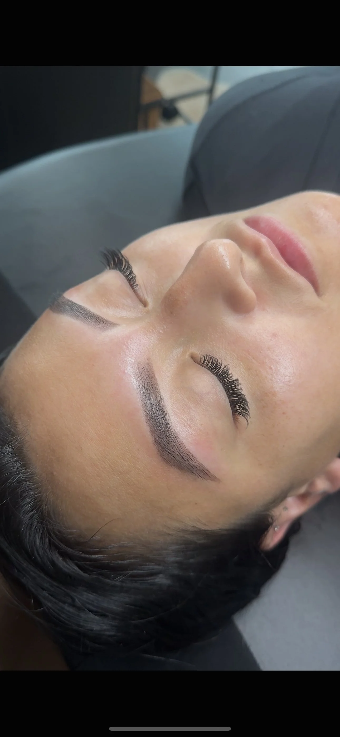 Close-up of a woman's face lying down with eyelash extensions and well-groomed eyebrows.