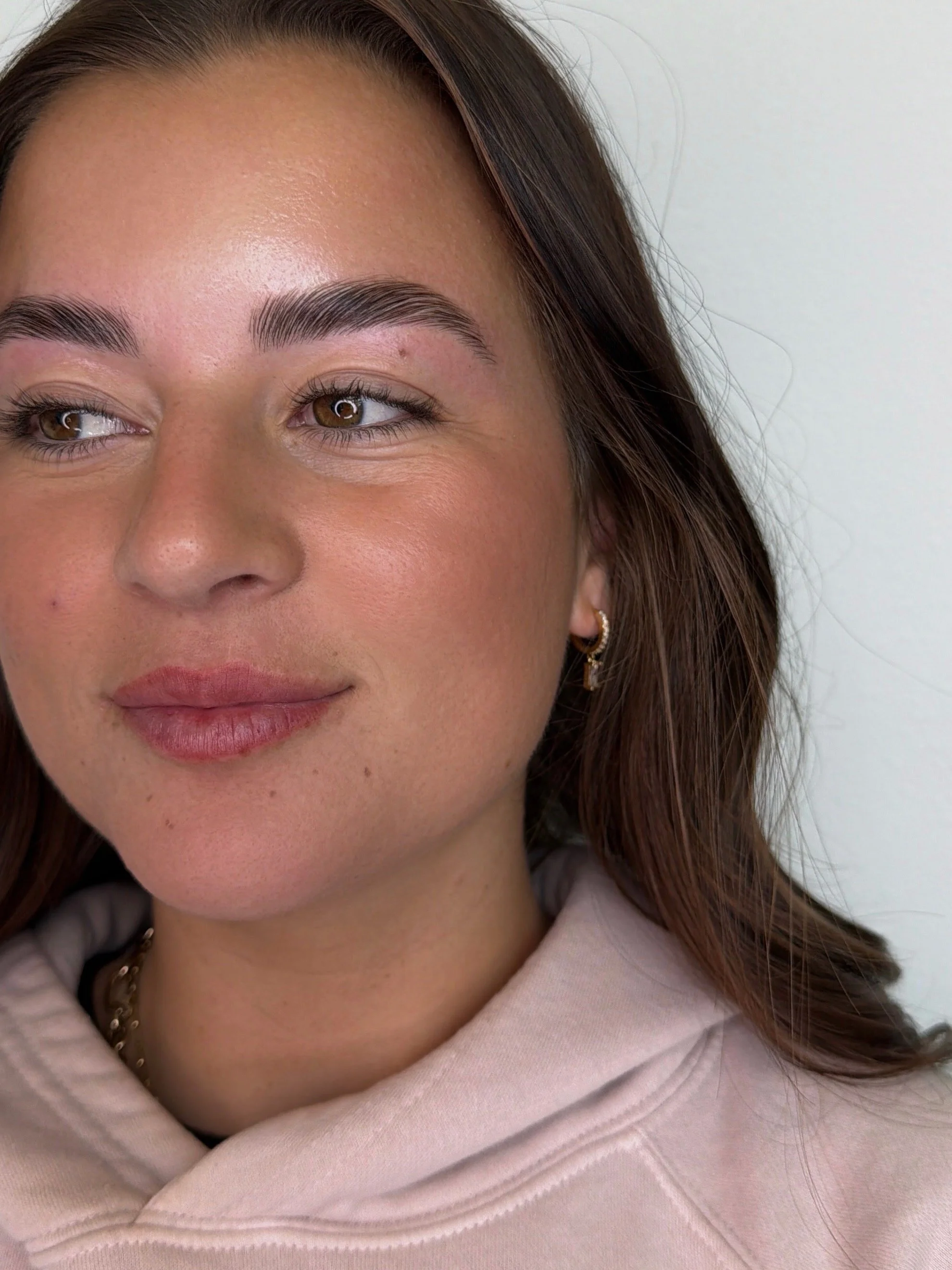 Close-up of a woman's face showing her eye, eyebrow, and part of her nose and lips. She has brown hair, tan skin, and is wearing a hoodie and earrings.