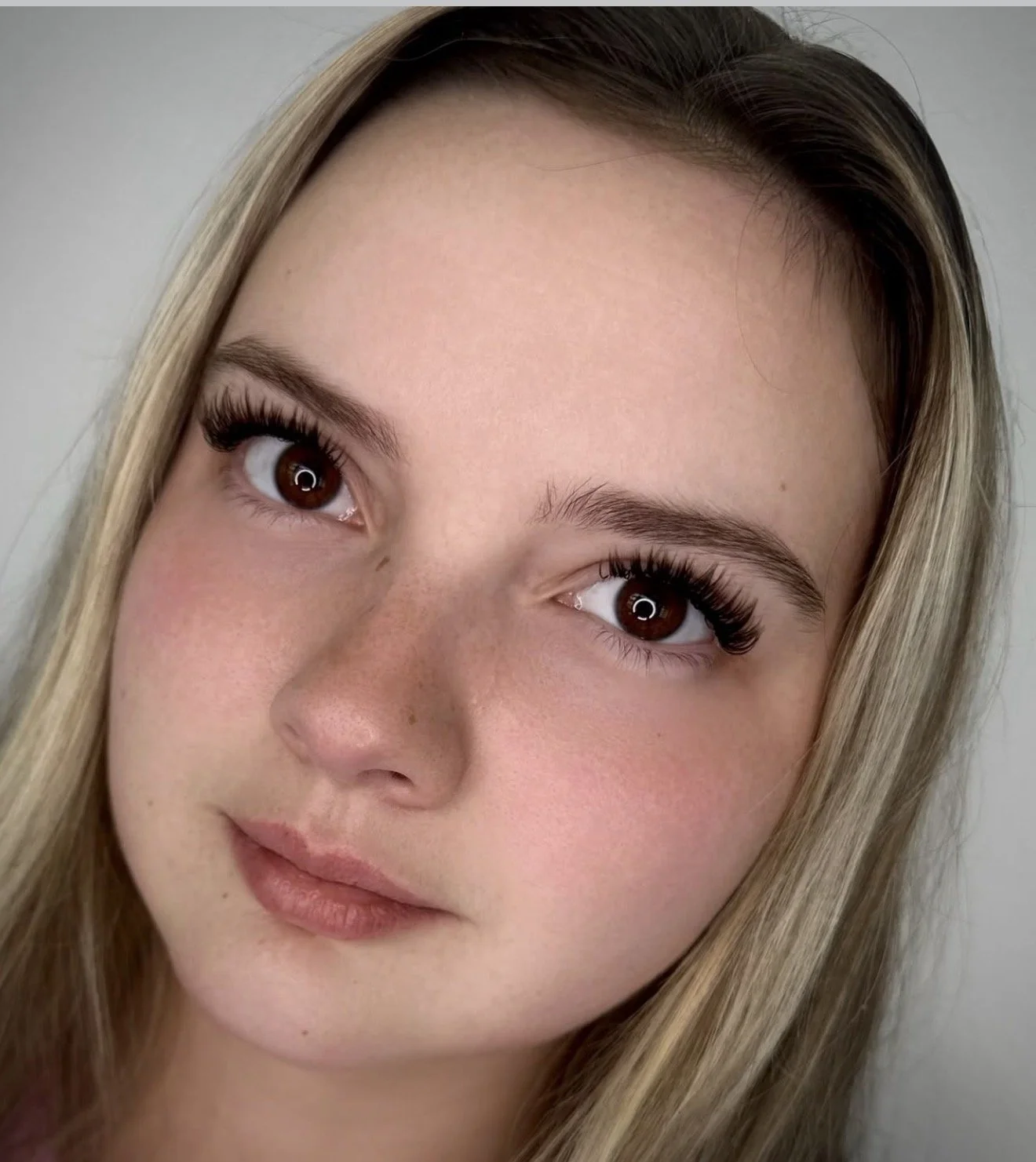 Close-up of a young woman's face showing her eyes, nose, and part of her lips, with long blonde hair and a neutral background.
