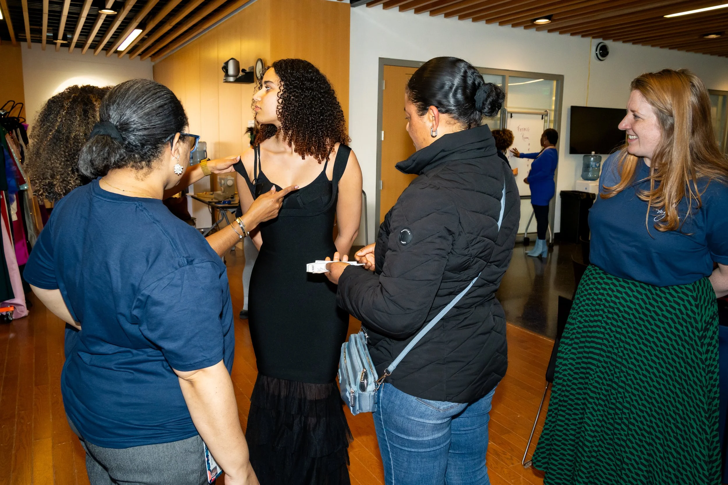 Boston Public Schools staff members and family members assist a student with a black formal dress. 
