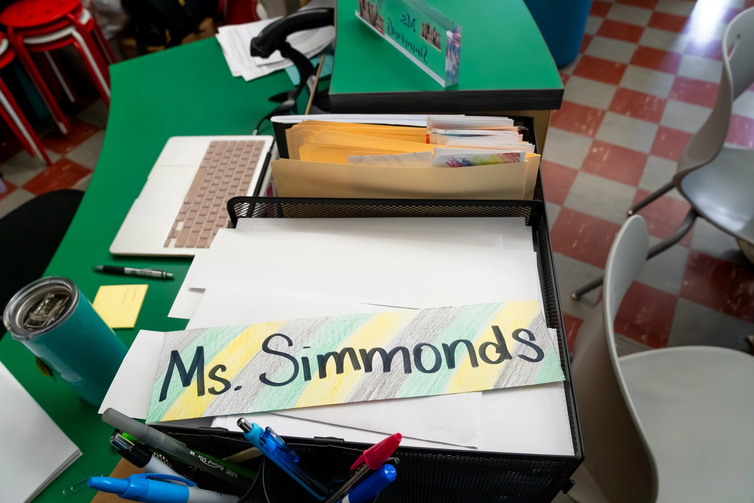 A colorful handwritten name tag for "Ms. Simmonds" lays on a desk.