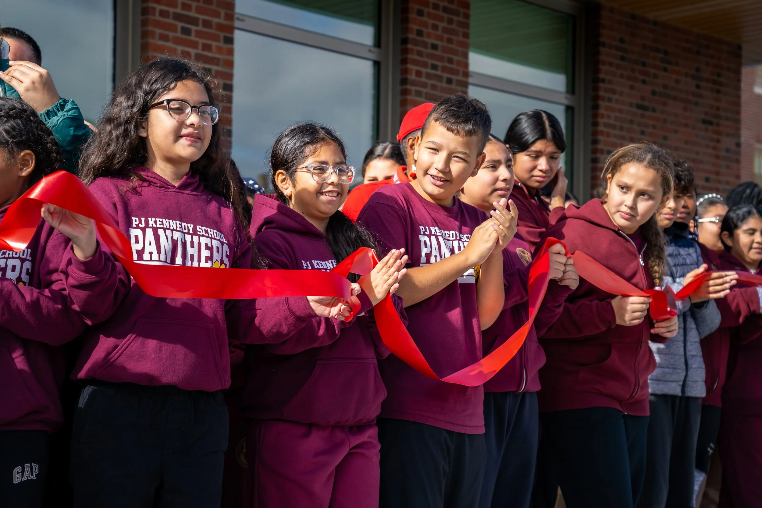 Patrick J Kennedy Elementary School students clap and cheer while holding a long red ribbon.