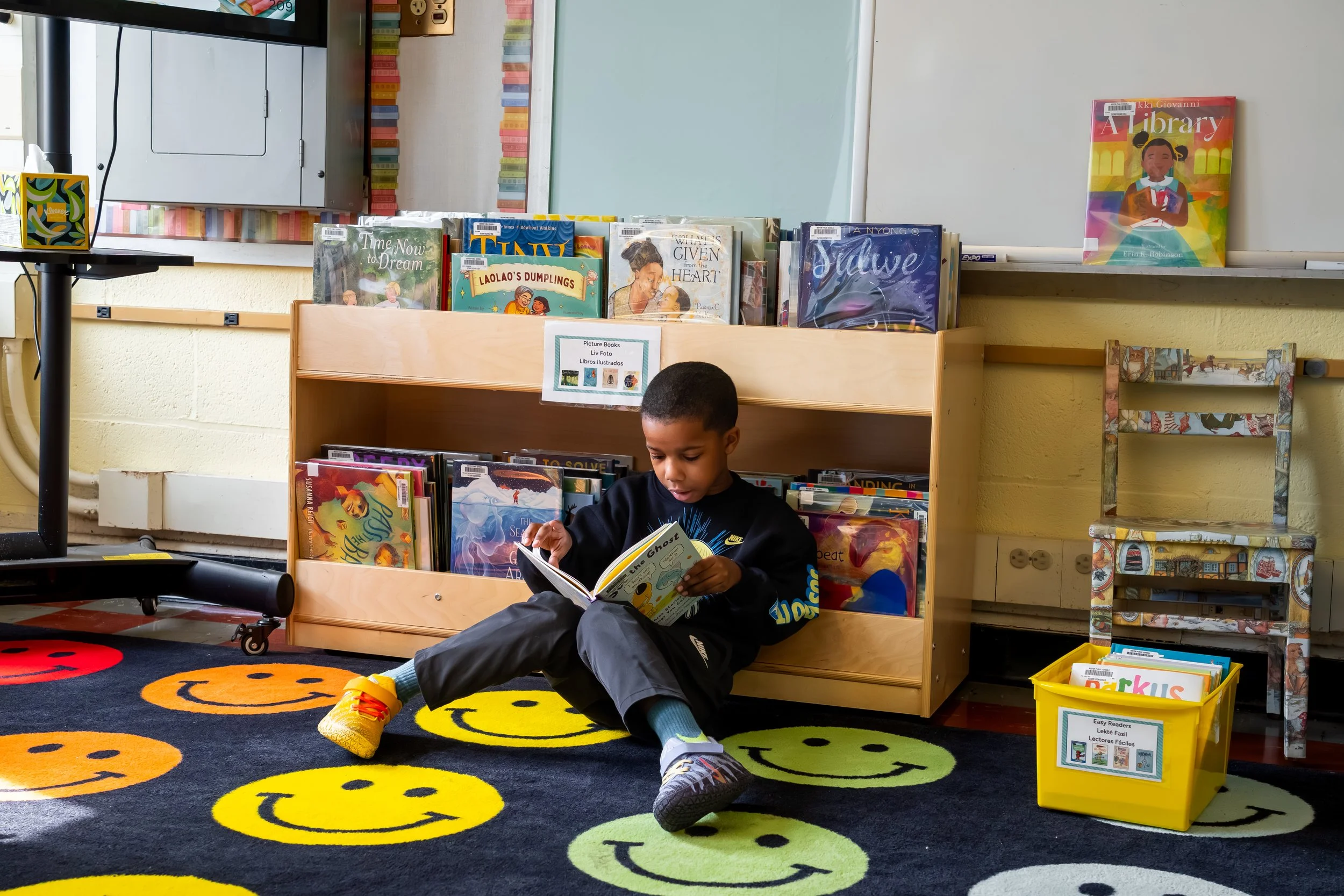 Boston Public Schools student sits on a rug  and reads a book at the Chittick Elementary School library.