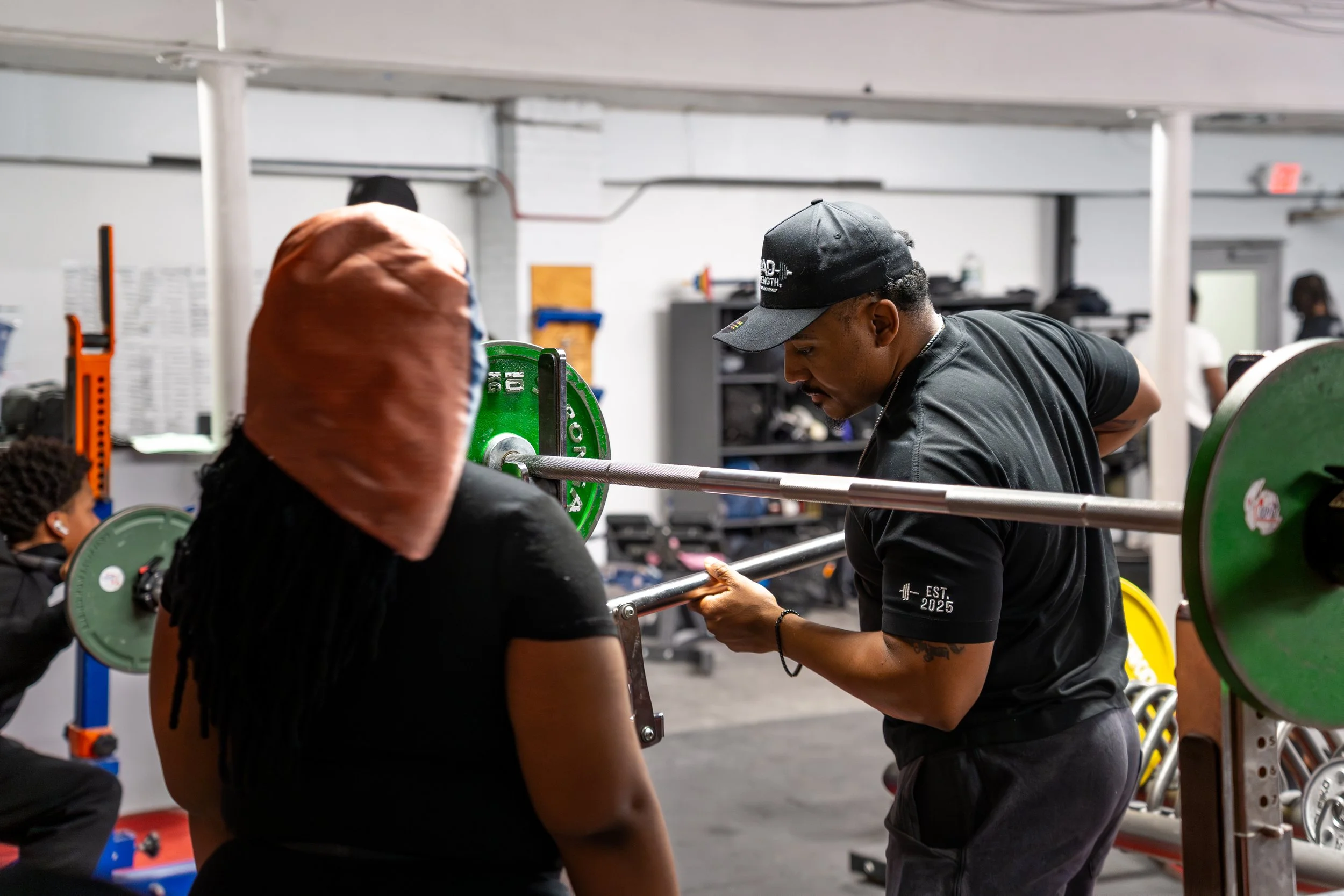 Boston Public Schools educator and power lifter Marcus Brown assists a student with reloading a bar bell.