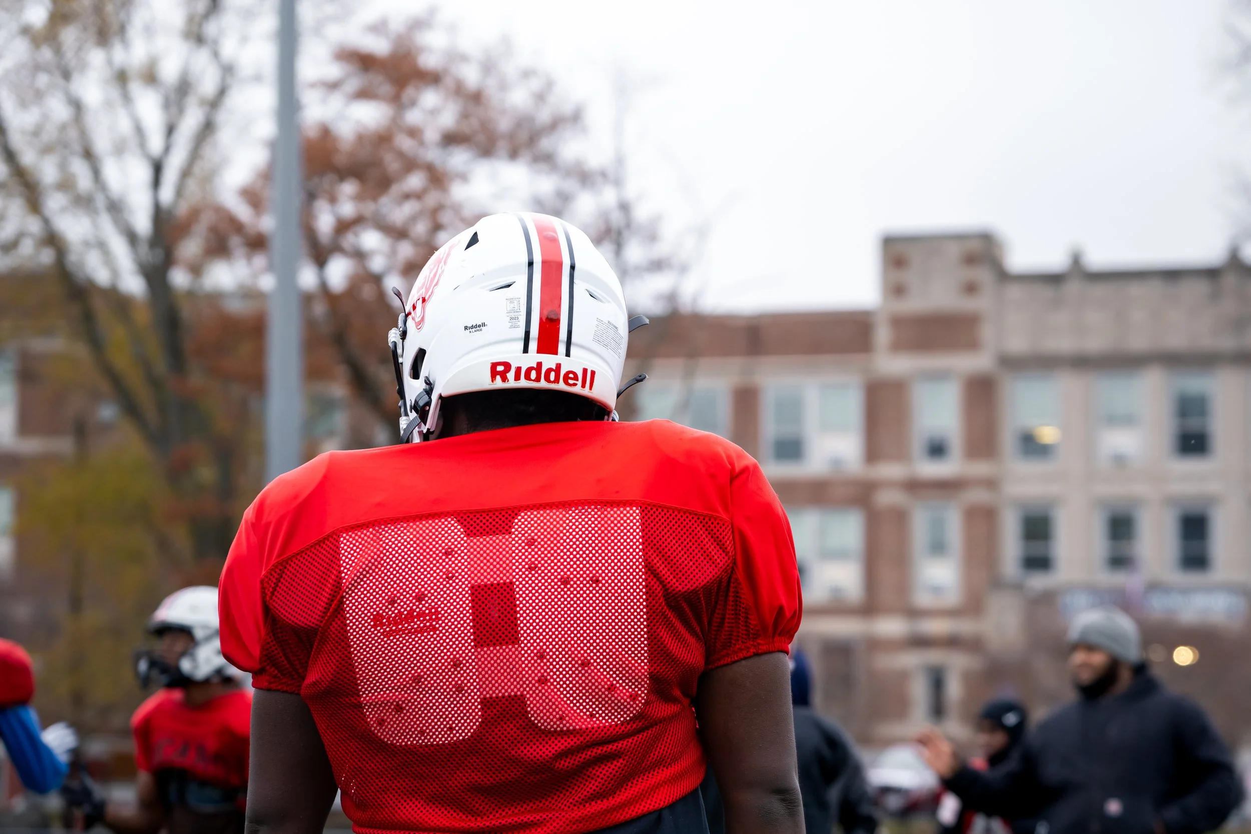 Boston Public Schools football player Edgar Santana Castro stands in uniform with TechBoston Academy in the background. 