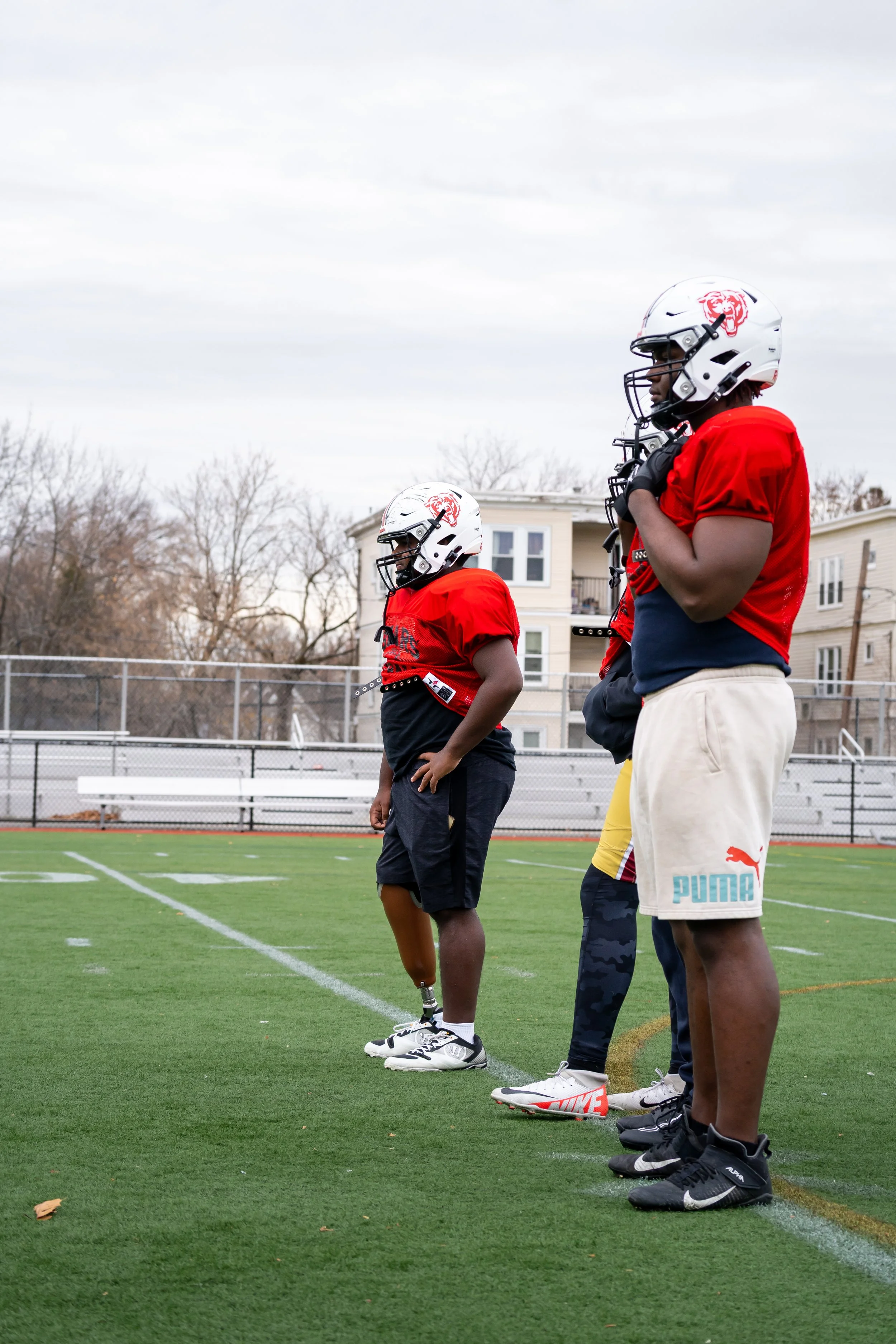 Boston Public Schools football player Edgar Santana Castro stands in uniform with two other players.