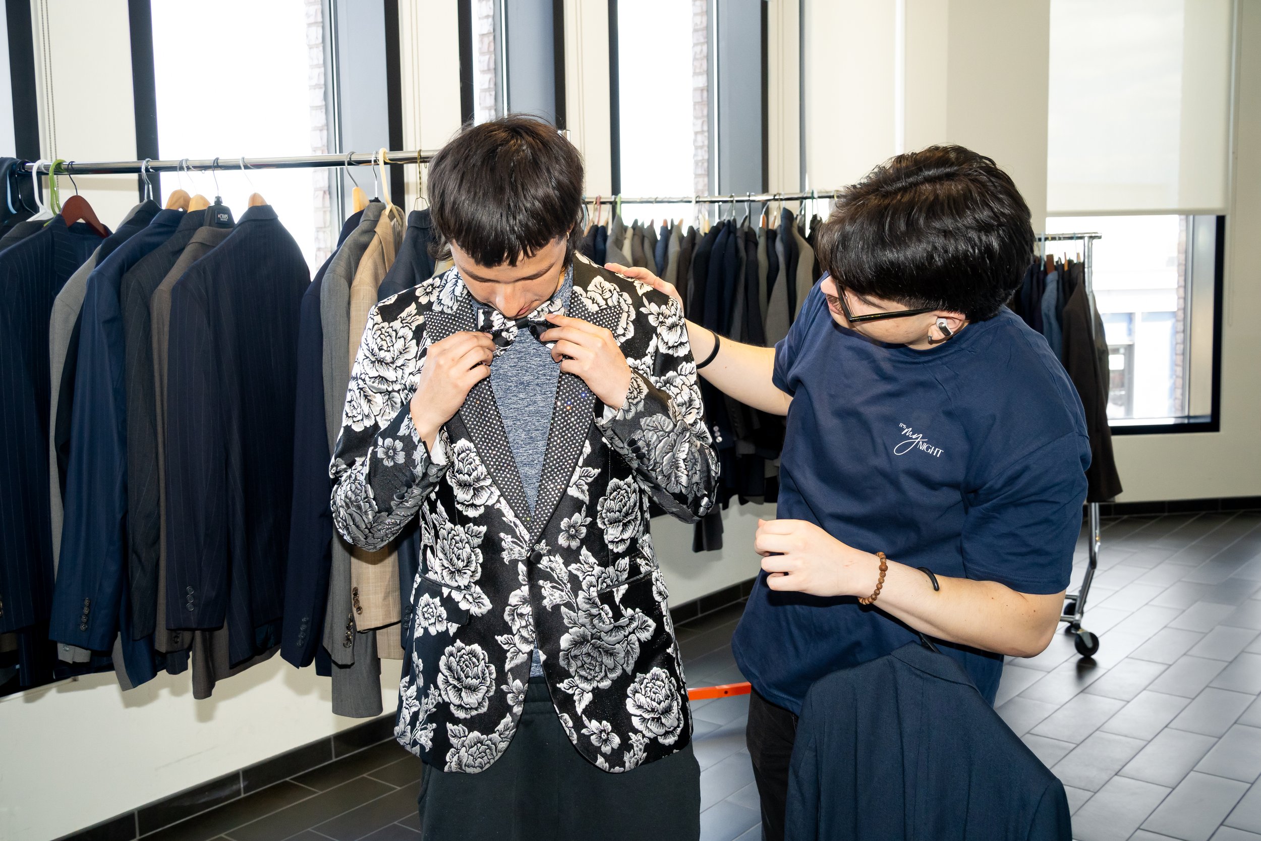 Boston Public Schools staff member assists a student with a black and white suit jacket. 
