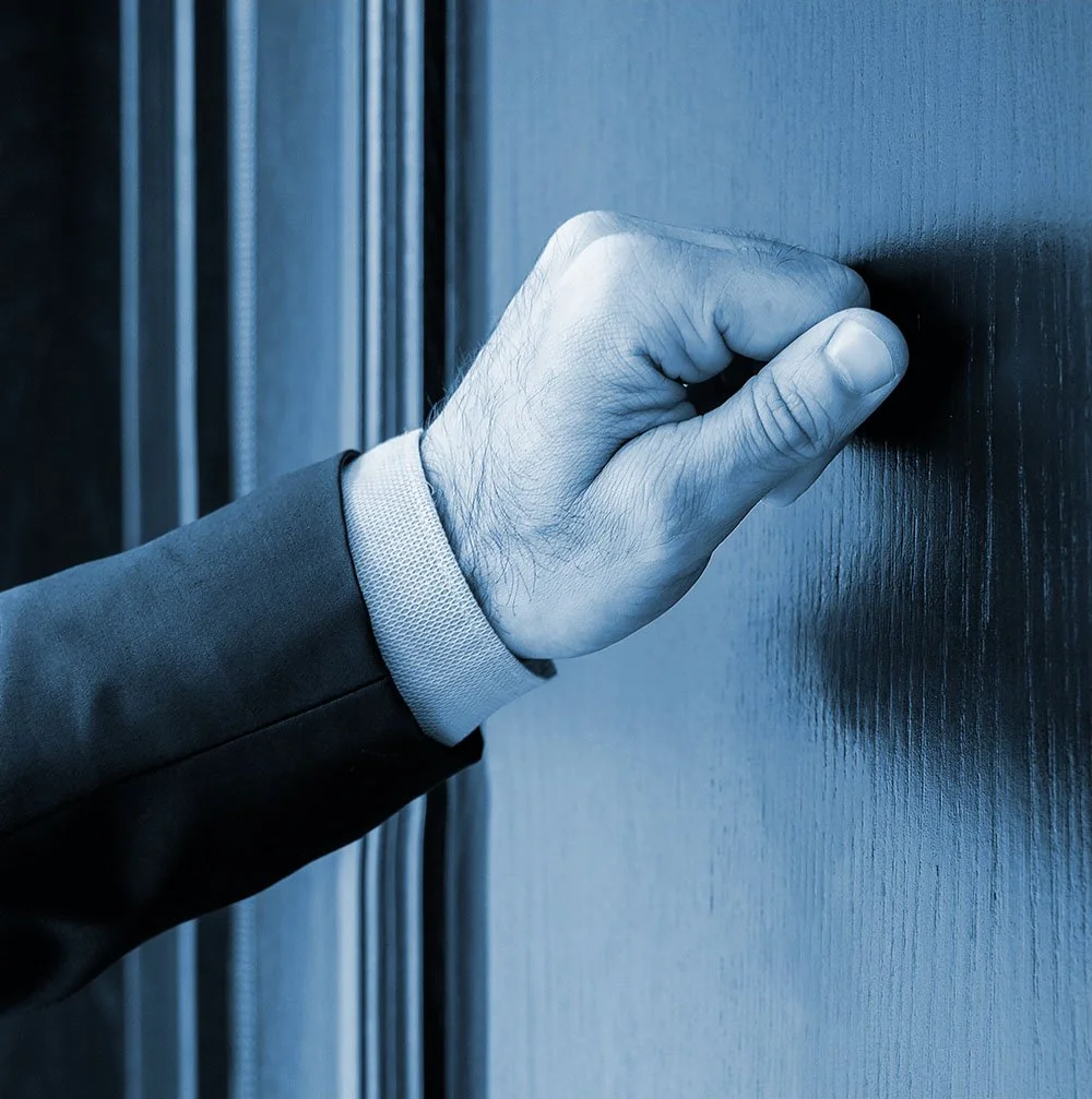 A man in a suit about to knock on a door with his fist.