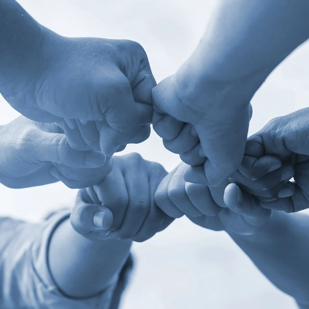 Four blue-gloved hands form a chain link, illustrating teamwork or unity.