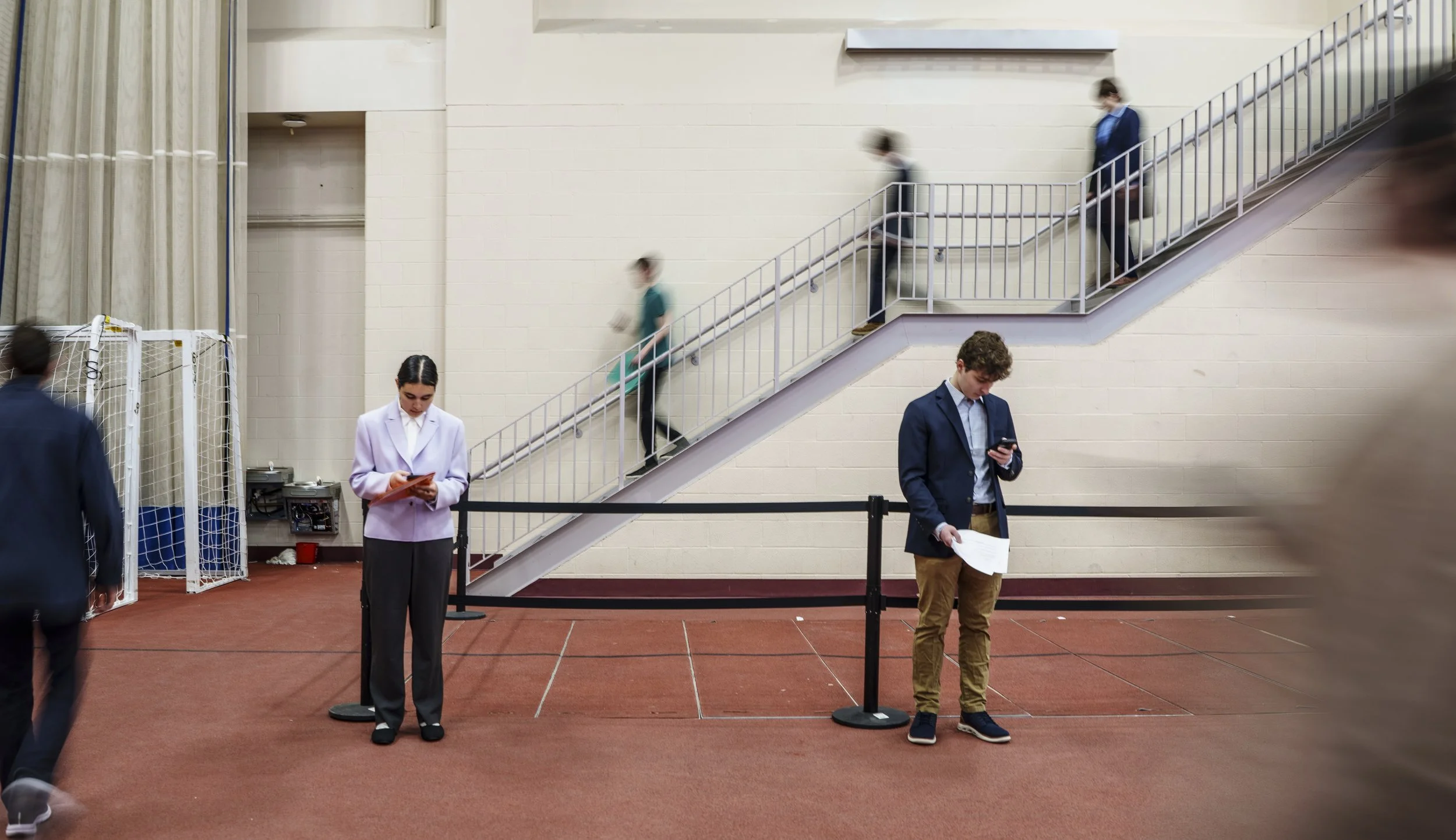 Students in the center look up which employer to meet with next as other students walk down the stairs into the event area of the Gordon Field House at Rochester Institute of Technology during the career fair Feb. 25, 2026.