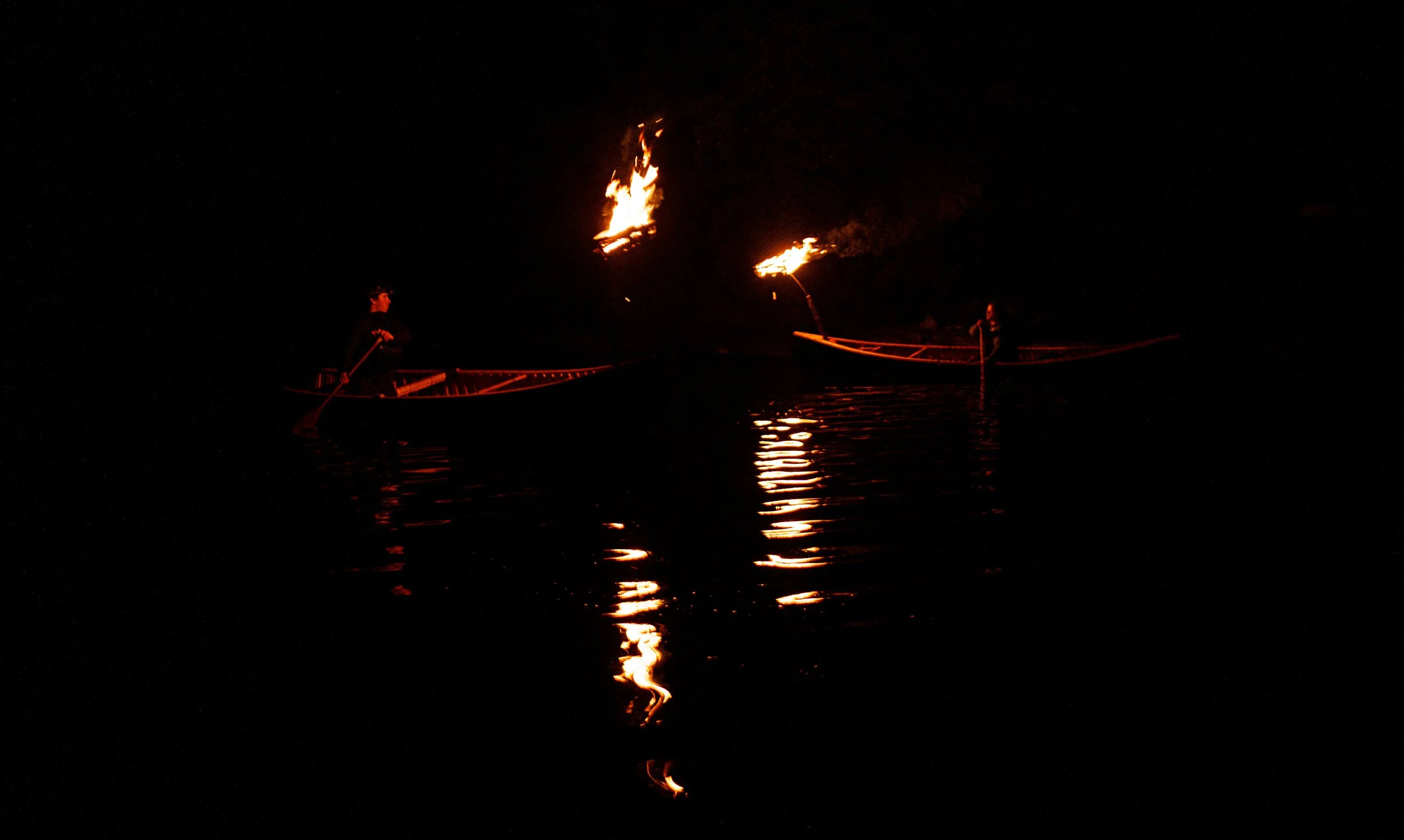 Left: Duncan Smith and Right: Sarah Berton paddle canoes fitted with small baskets containing kindling in the ritual canoe ballet performance hosted by Camp Temagami at the conclusion of the summer of wilderness canoe trips, Aug 8, 2026