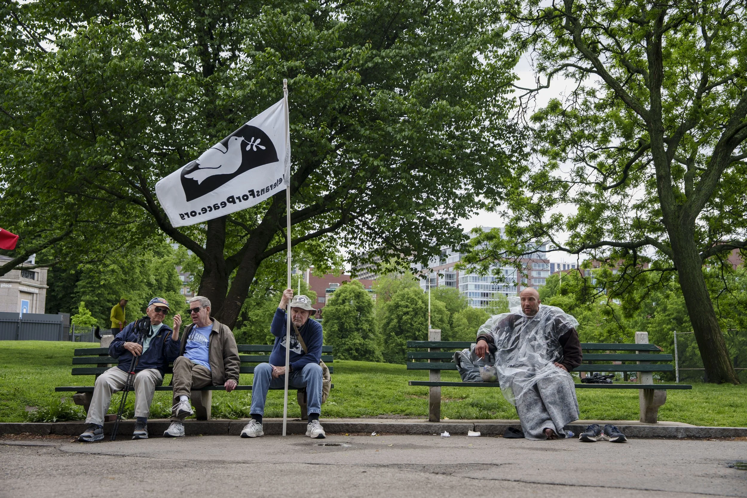 A demonstrator holds a Veterans for Peace flag on a park bench in the Boston Common, surrounded by members of the public on May 25, 2026