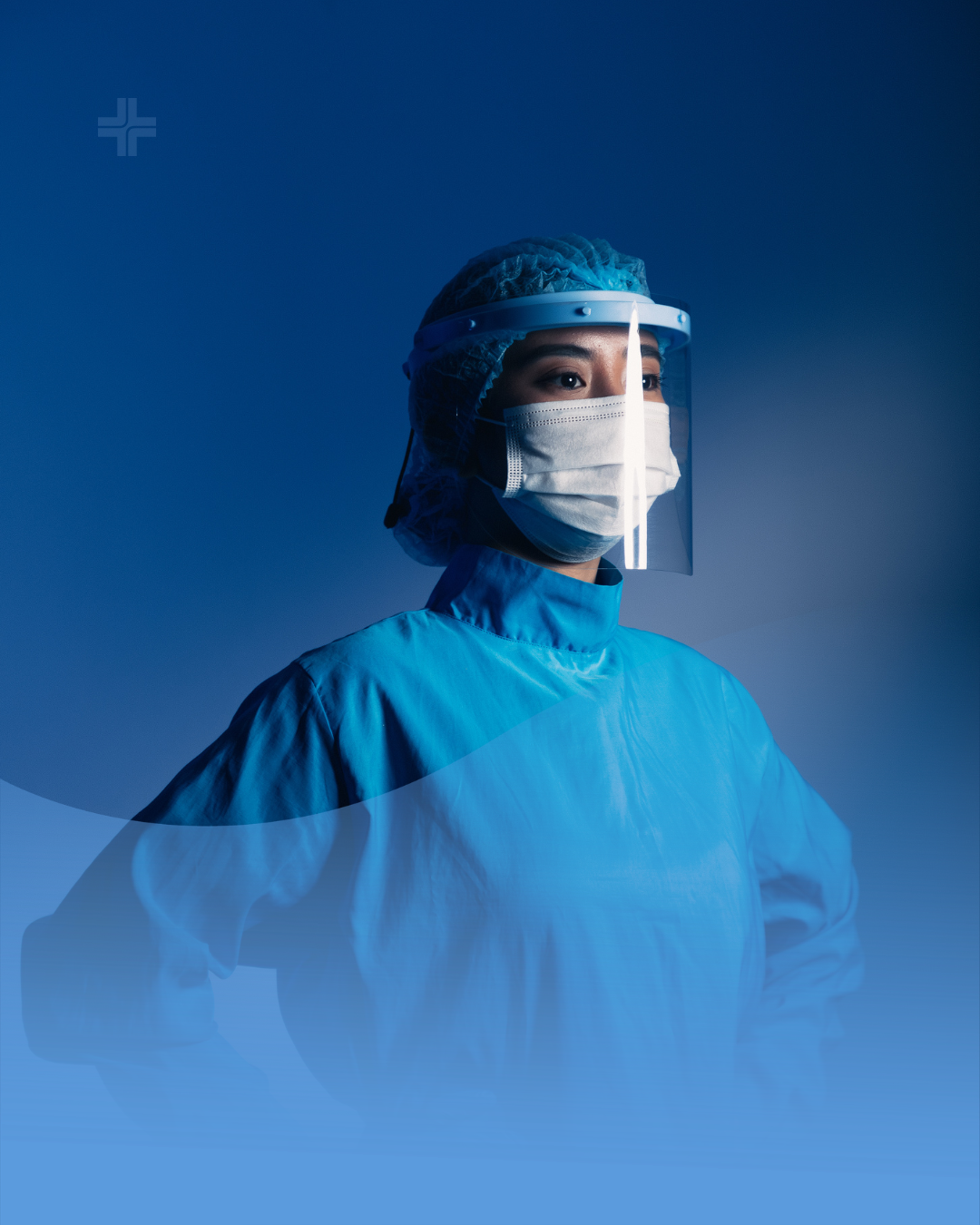 Female healthcare worker in blue medical gown, face mask, surgical cap, and clear face shield looking to the side against a dark blue background.