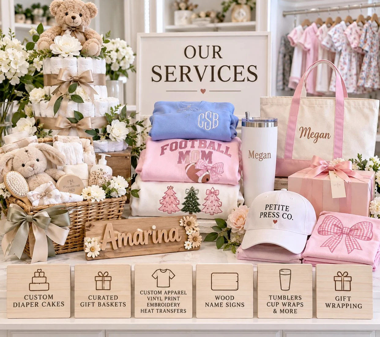 Display of baby shower gifts, including embroidered clothing, plush toys, gift baskets, a tote bag labeled with a name, a cap, and wrapped presents, arranged behind a sign that says "Our Services" in a retail store with clothing on hangers in the background.