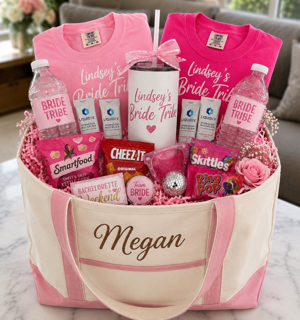 Gift basket for a bride, including personalized water bottles labeled 'Bride Tribe,' pink and white shirts reading 'Lindsey's Bride Tribe,' snacks like Smartfood popcorn, Skittles, Cheez-It, and Ring Pop, a pink rose, a small silver golf ball, pink sunglasses, and various wedding-themed decorations inside a pink and white bag with the name 'Megan' embroidered on it.