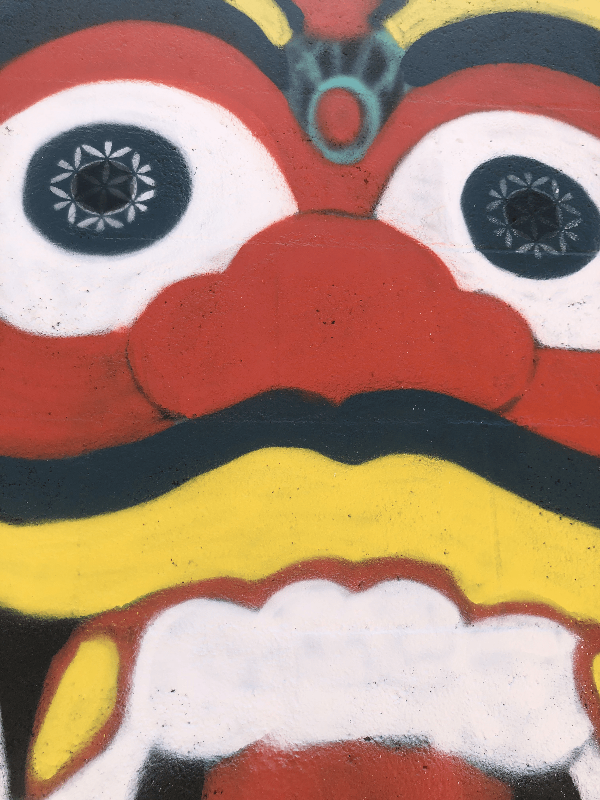 Close-up of a colorful graffiti mural featuring a Indonesian Barong Mask stylized with large eyes, red nose, and a mustache, painted on a wall.