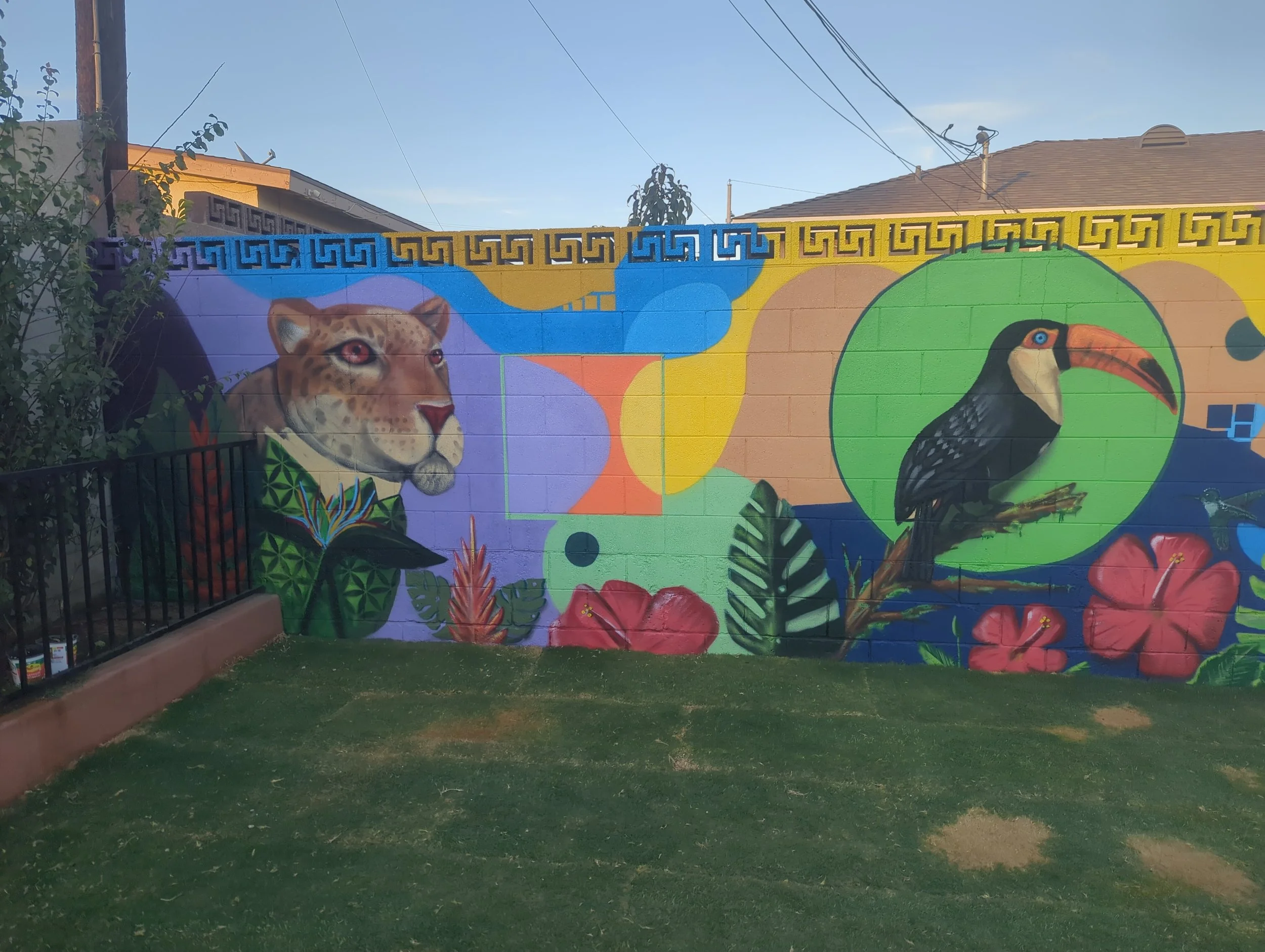 Colorful mural on a wall depicting a Jaguar and a toucan bird in a vibrant, abstract nature scene with large green leaves and red hibiscus flowers.