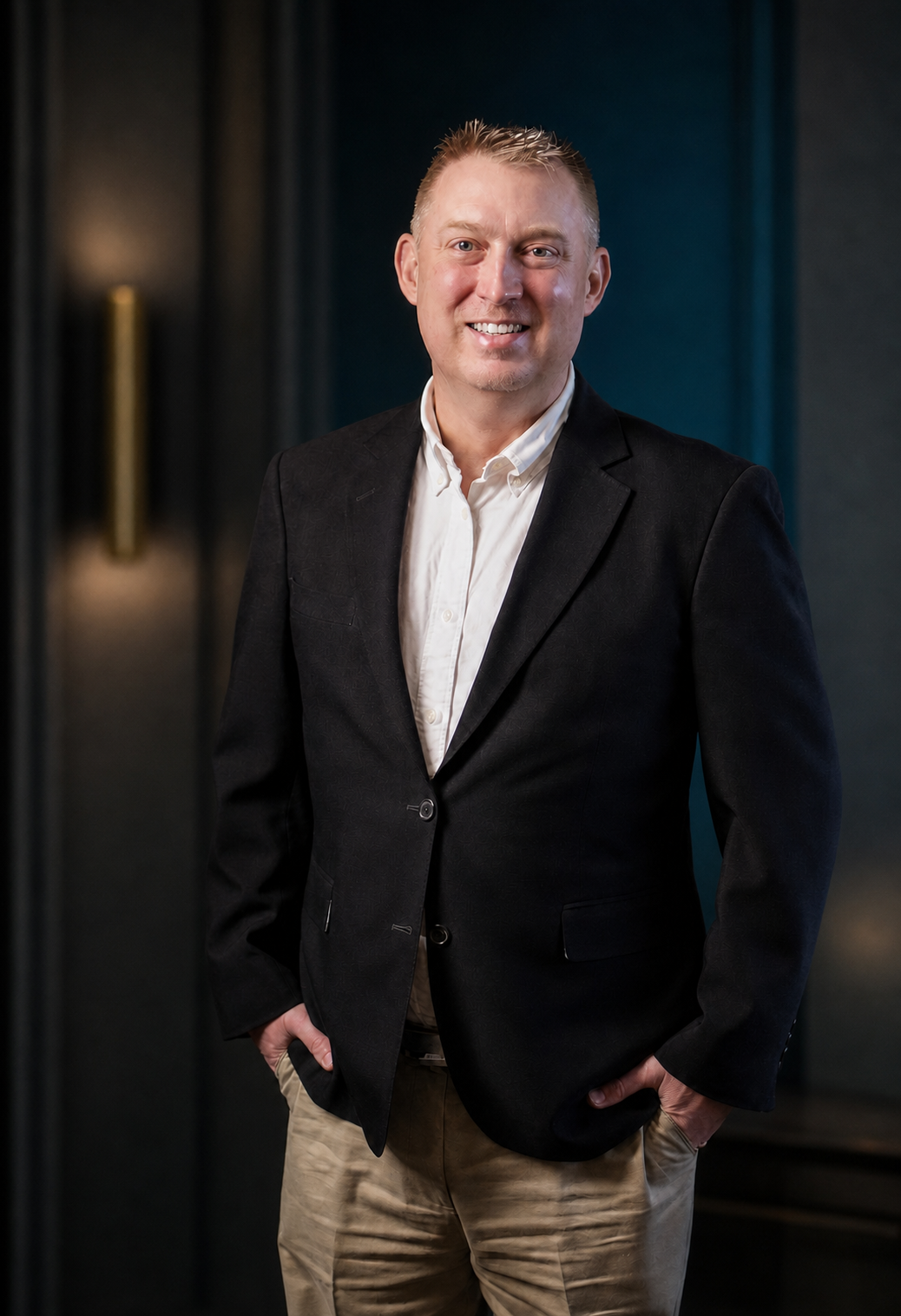 Portrait of the founder of Corvenay Holdings in a black blazer against a deep teal and charcoal background