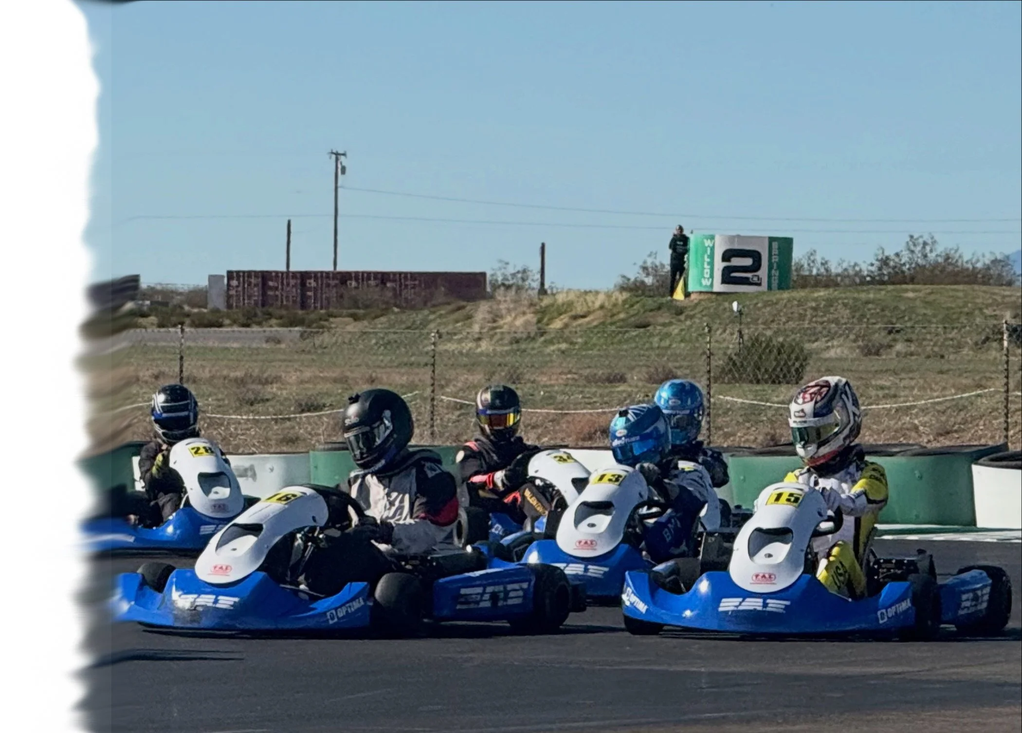 Group of people wearing helmets seated on go-kart vehicles at a race track, preparing for a race.