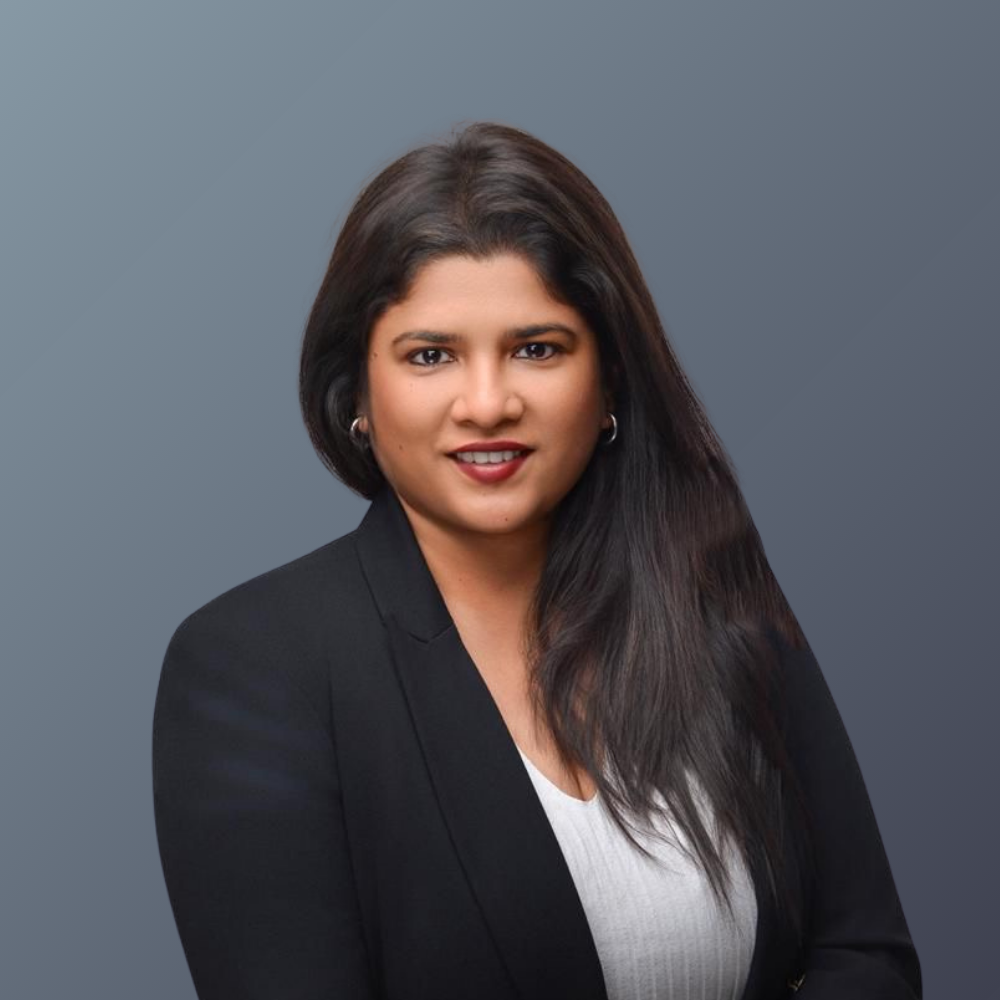 Professional woman with long dark hair wearing a black blazer and white top against a gray background.