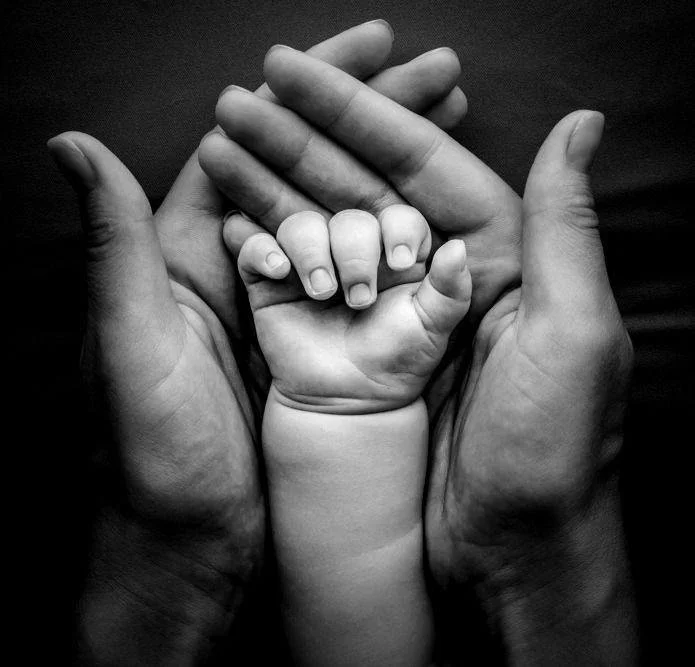 Une famille avec des mains d'adultes tenant une petite main d'enfant, symbolisant le lien familial et la protection.