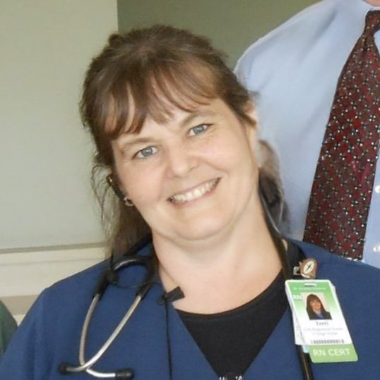 A smiling woman in a nurse's uniform with a stethoscope and a hospital ID badge.