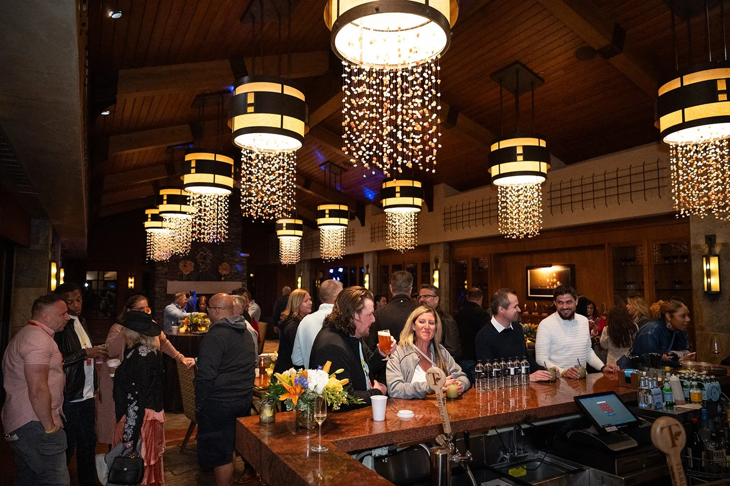 People gathering at a Tucson restaurant with elegant lighting fixtures, including hanging chandeliers and scattered guests socializing.