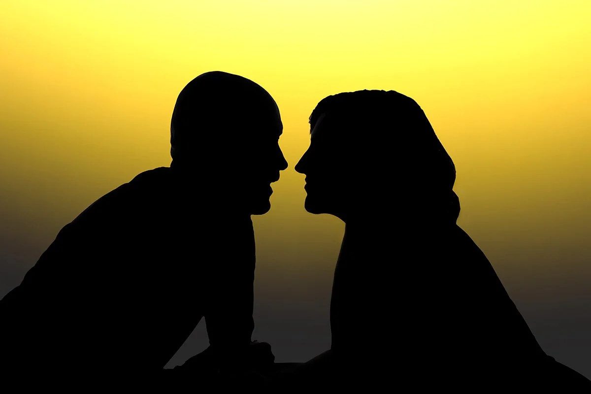 Silhouettes of a man and woman facing each other, with a yellow and orange gradient sky in the background during their branding photo shoot in Tucson, Arizona