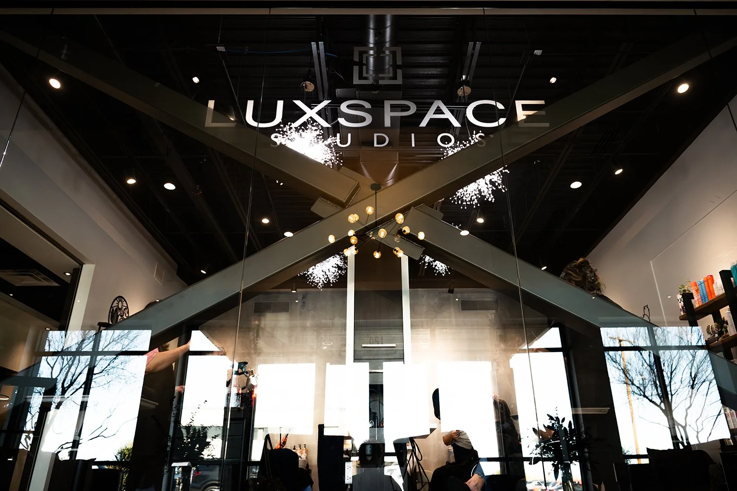Interior view of LuxSpace Studio salon with modern lighting, glass windows, and reflection of trees outside.
