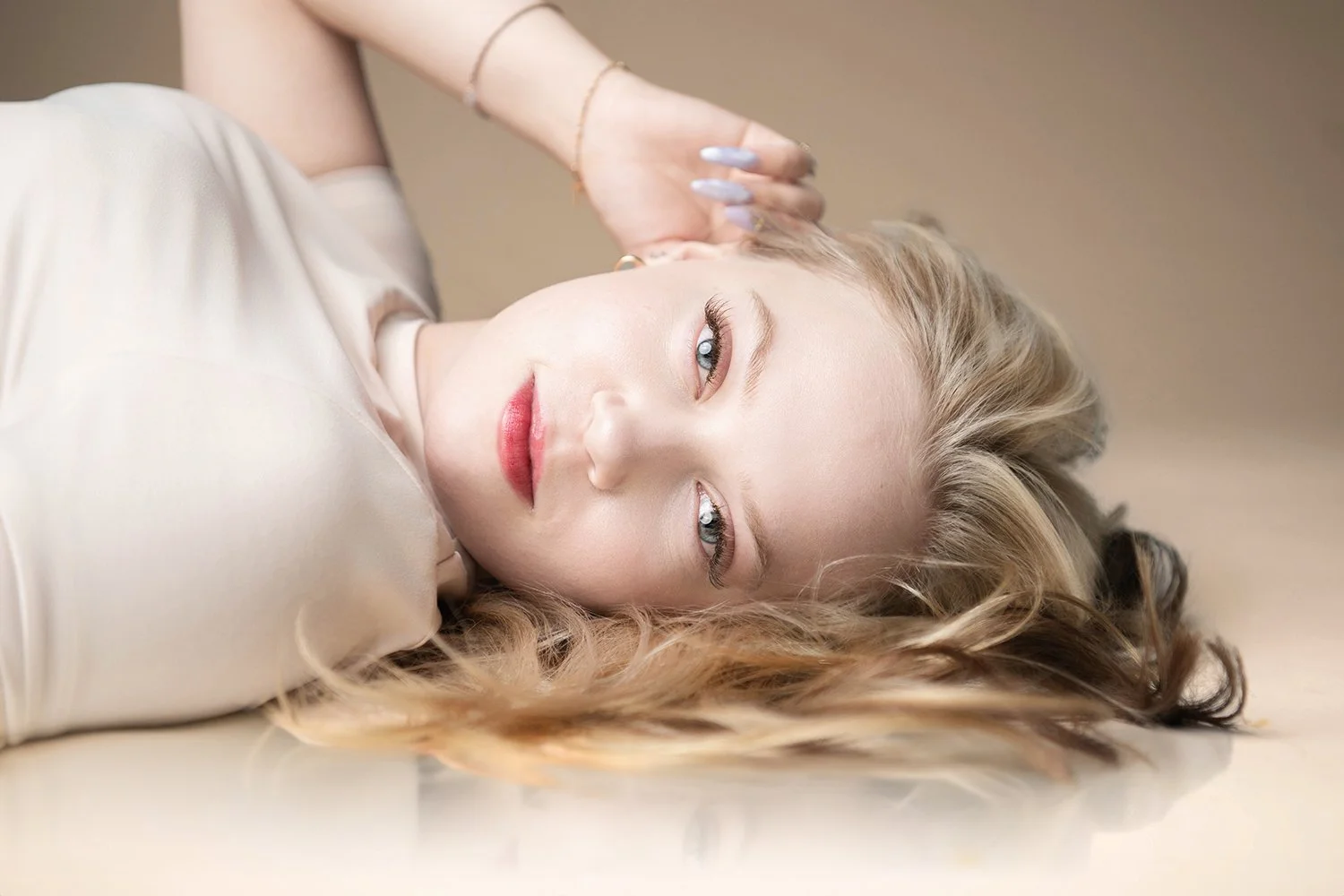 A young woman with blonde hair lying on her side on a bed, looking at the camera with a relaxed expression during a photo shoot at Amy Ijams Photography studio in Tucson, Az