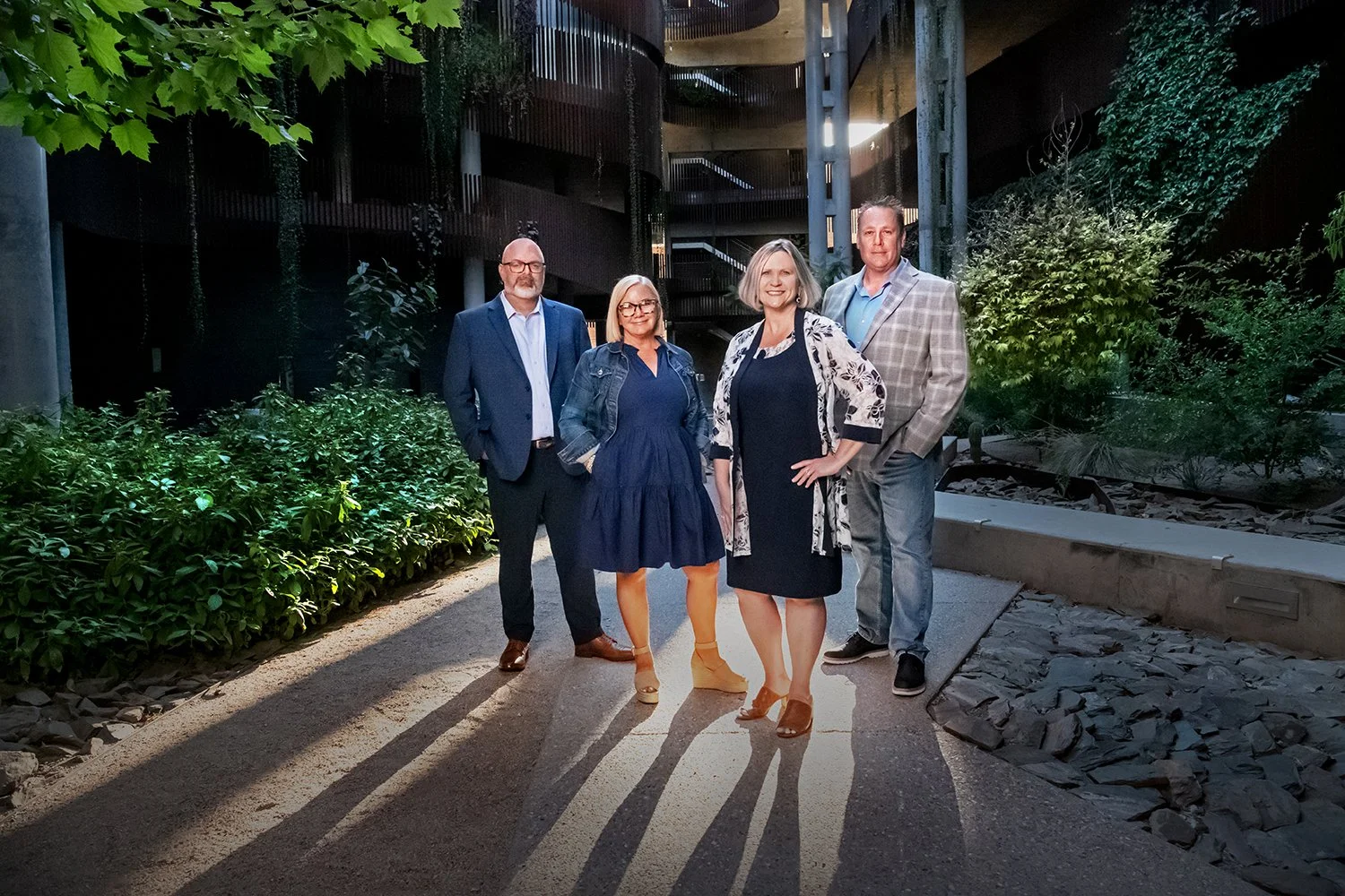 A group of five real estate agents standing on a pathway outdoors, with greenery and a modern building at University Arizona in the background during their brand photo shoot