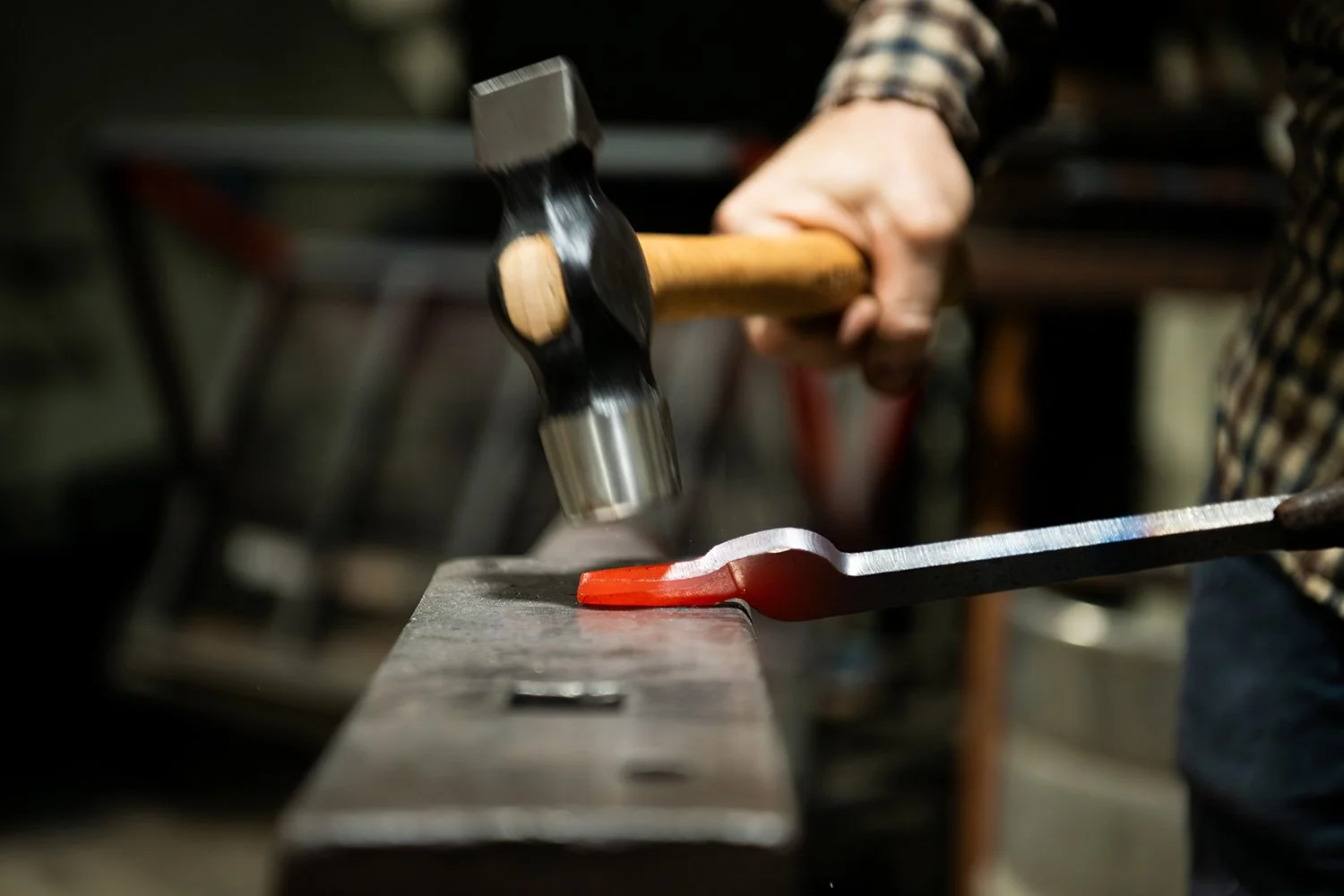 A person using a hammer to shape a piece of heated metal on an anvil in a blacksmith workshop.