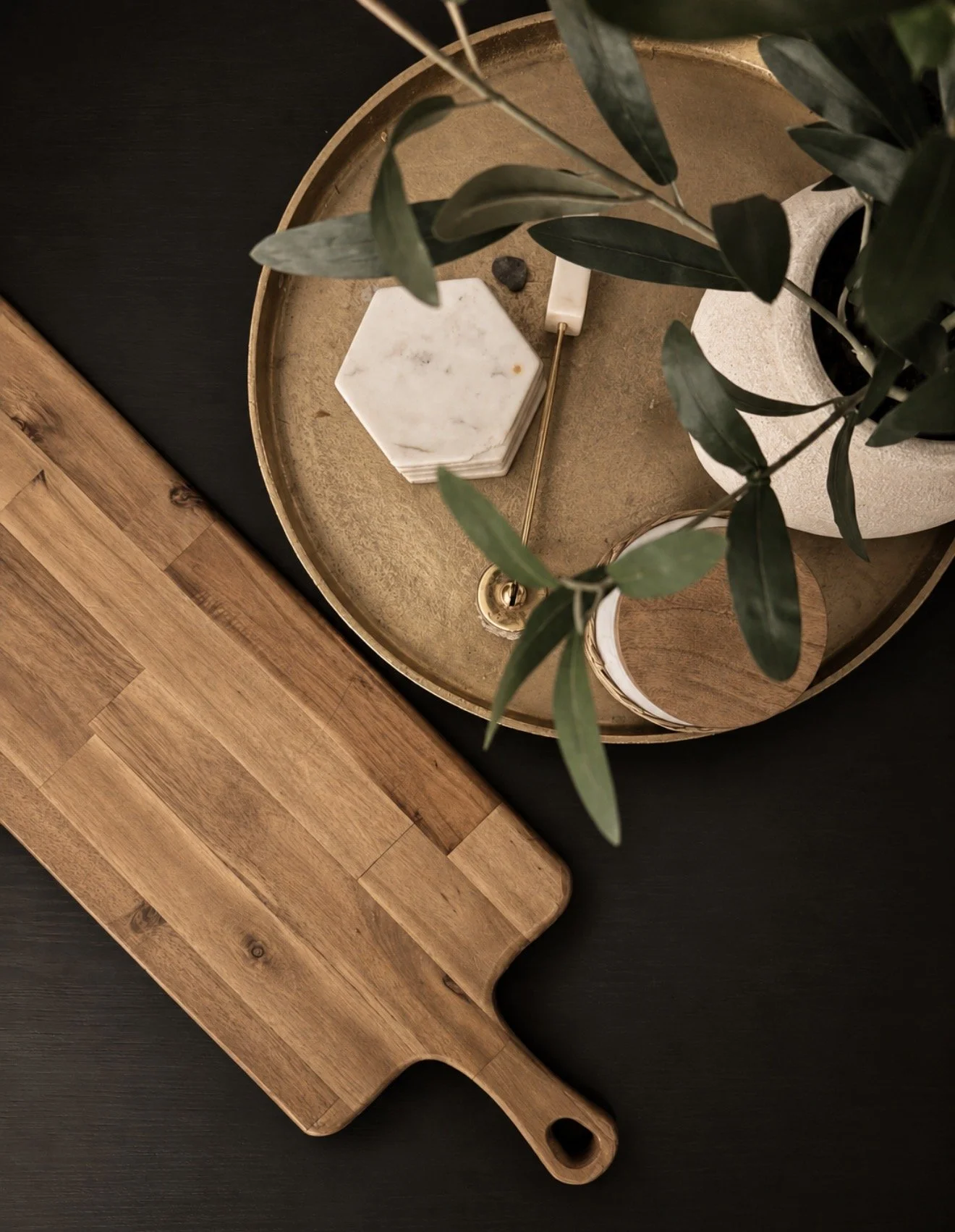 Wood serving board and brass tray styled with greenery on a black counter
