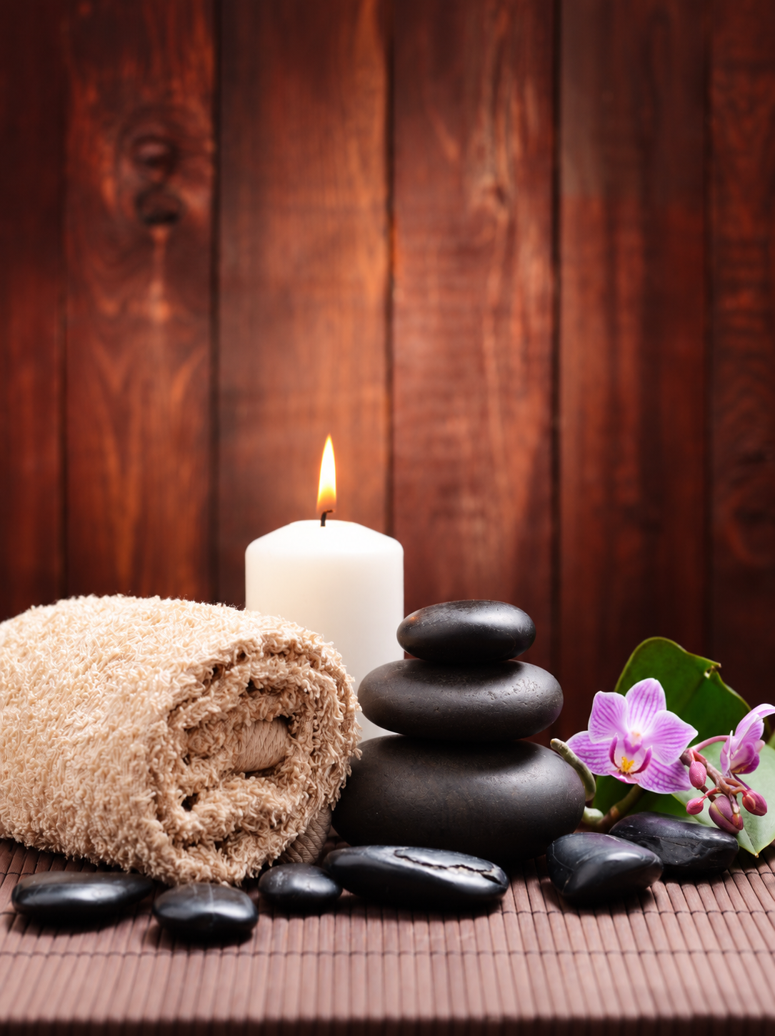 Massage therapy essentials with warm candlelight, hot stones, soft towel, and orchid in a relaxing spa setting.
