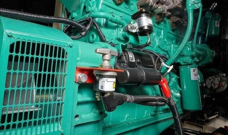 Close-up of a teal-colored industrial engine with various hoses, tubes, and mechanical parts.