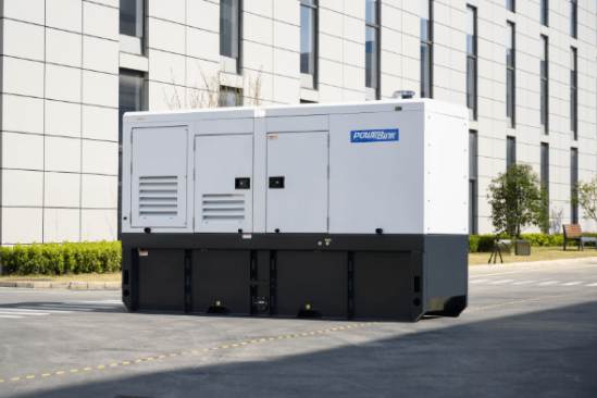 Large white and black portable generator unit on a city street with a modern building and some green bushes in the background.